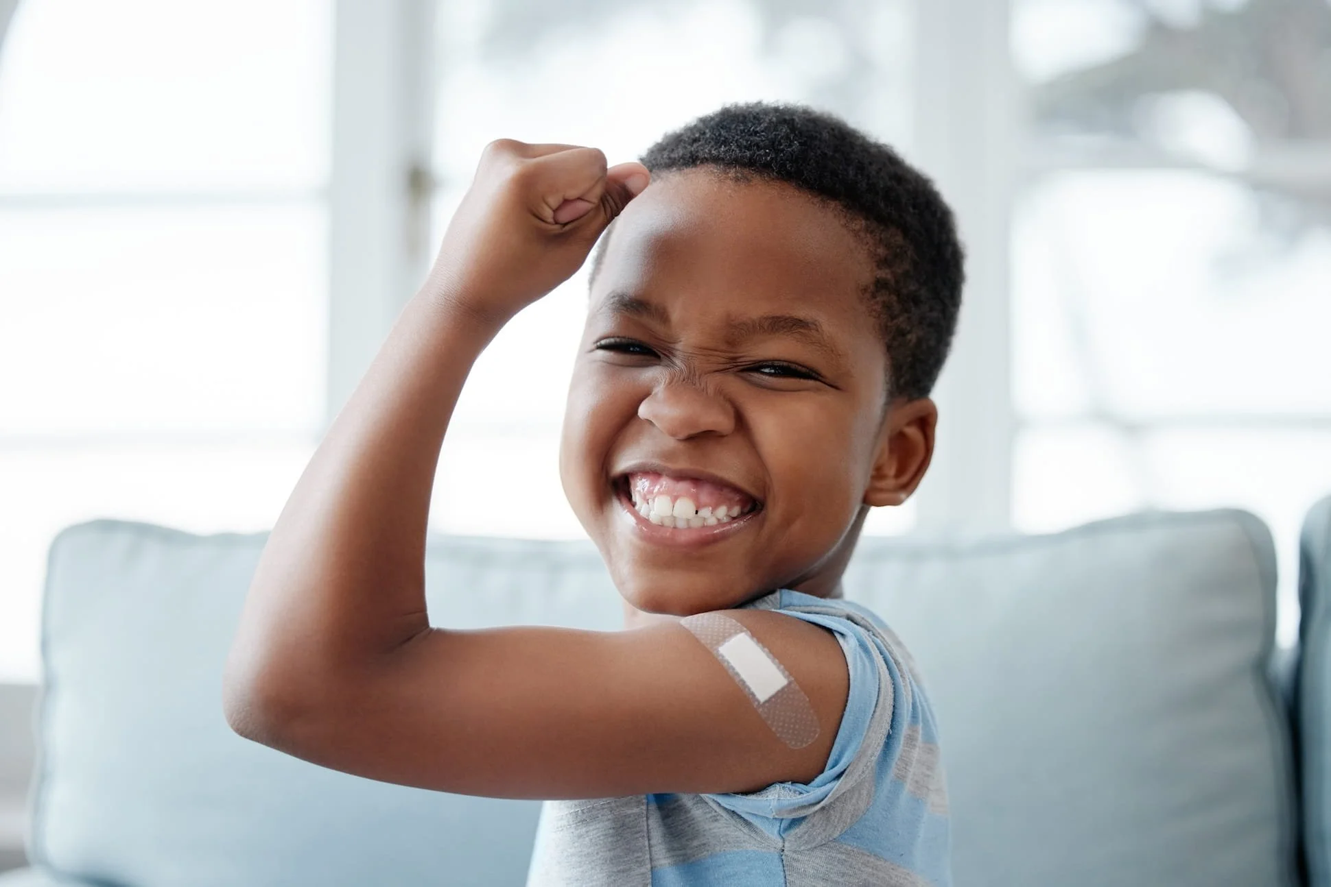 Young boy with a bandage on his upper arm smiling and flexing his bicep.
