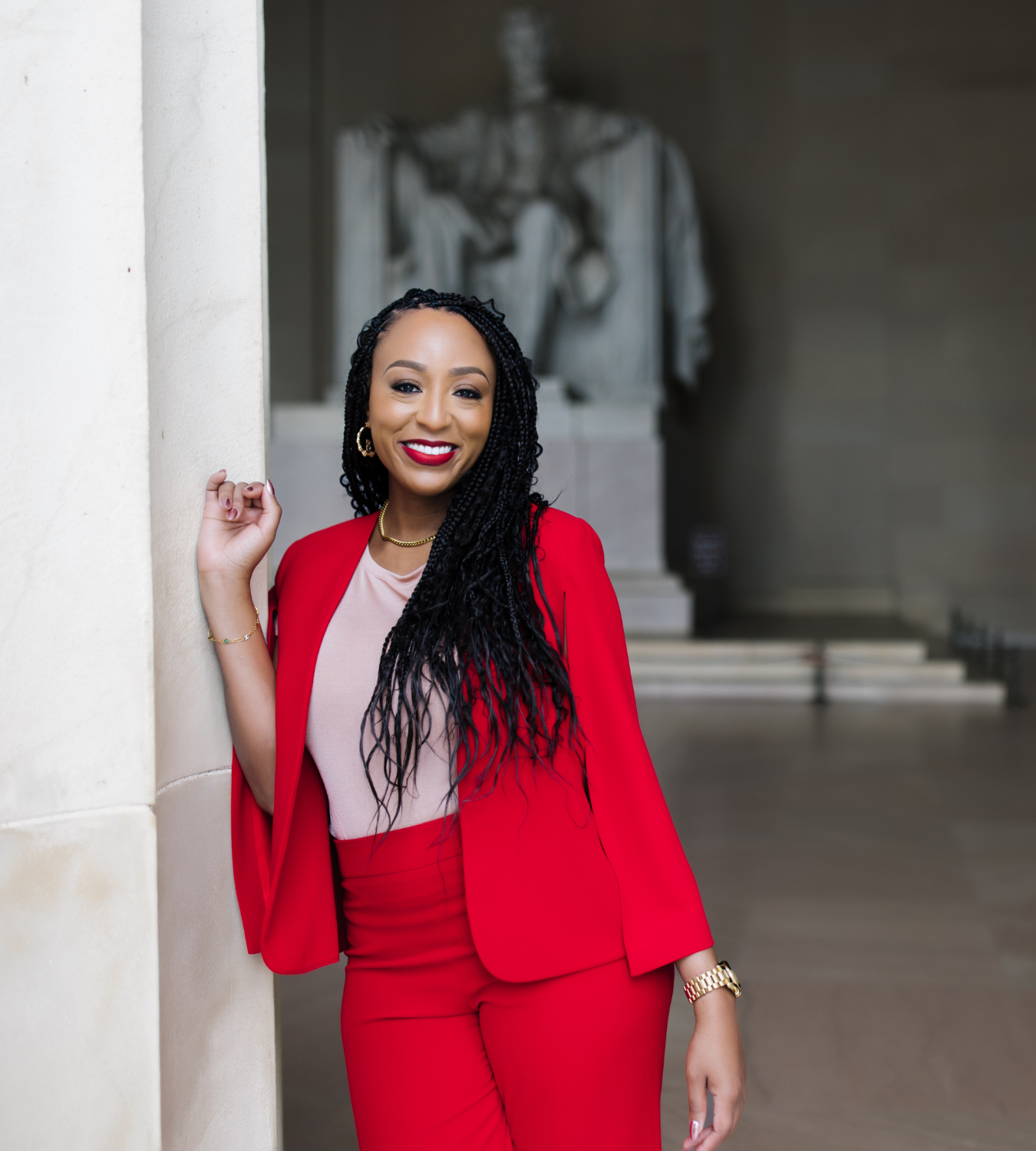 A woman dressed in a red blazer and red pants standing in a museum, smiling with a statue in the background.
