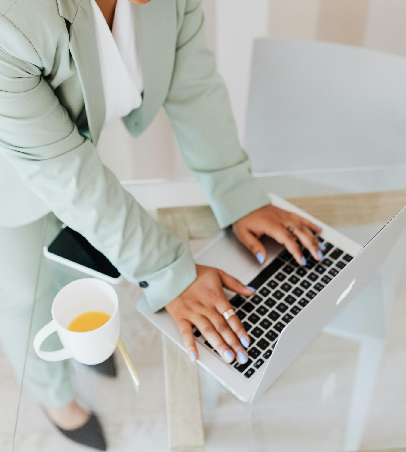 Person working on a laptop at a glass table with a cup of coffee nearby.
