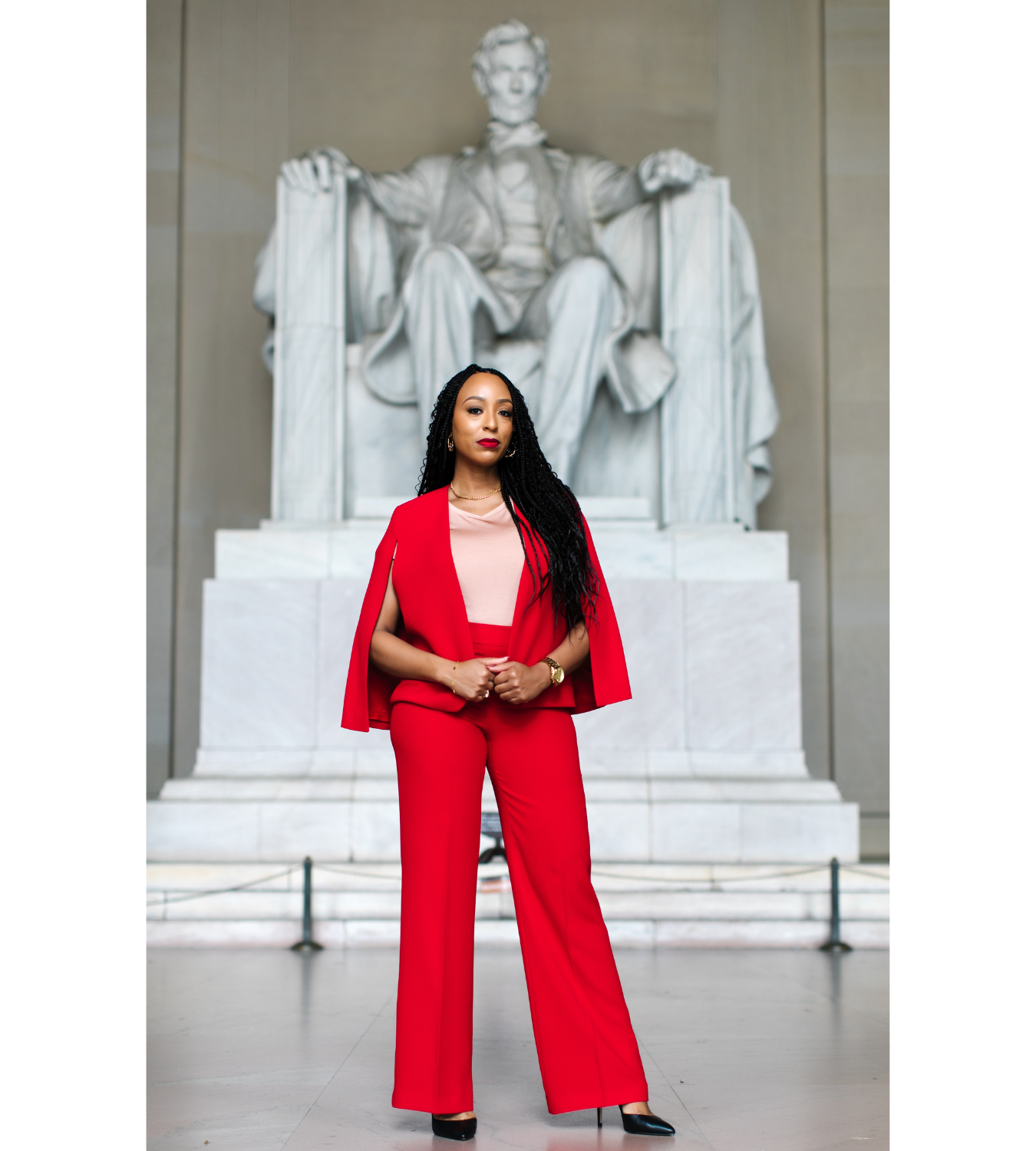 A woman in a red suit standing in front of the Lincoln Memorial, with the statue of Lincoln visible behind her.