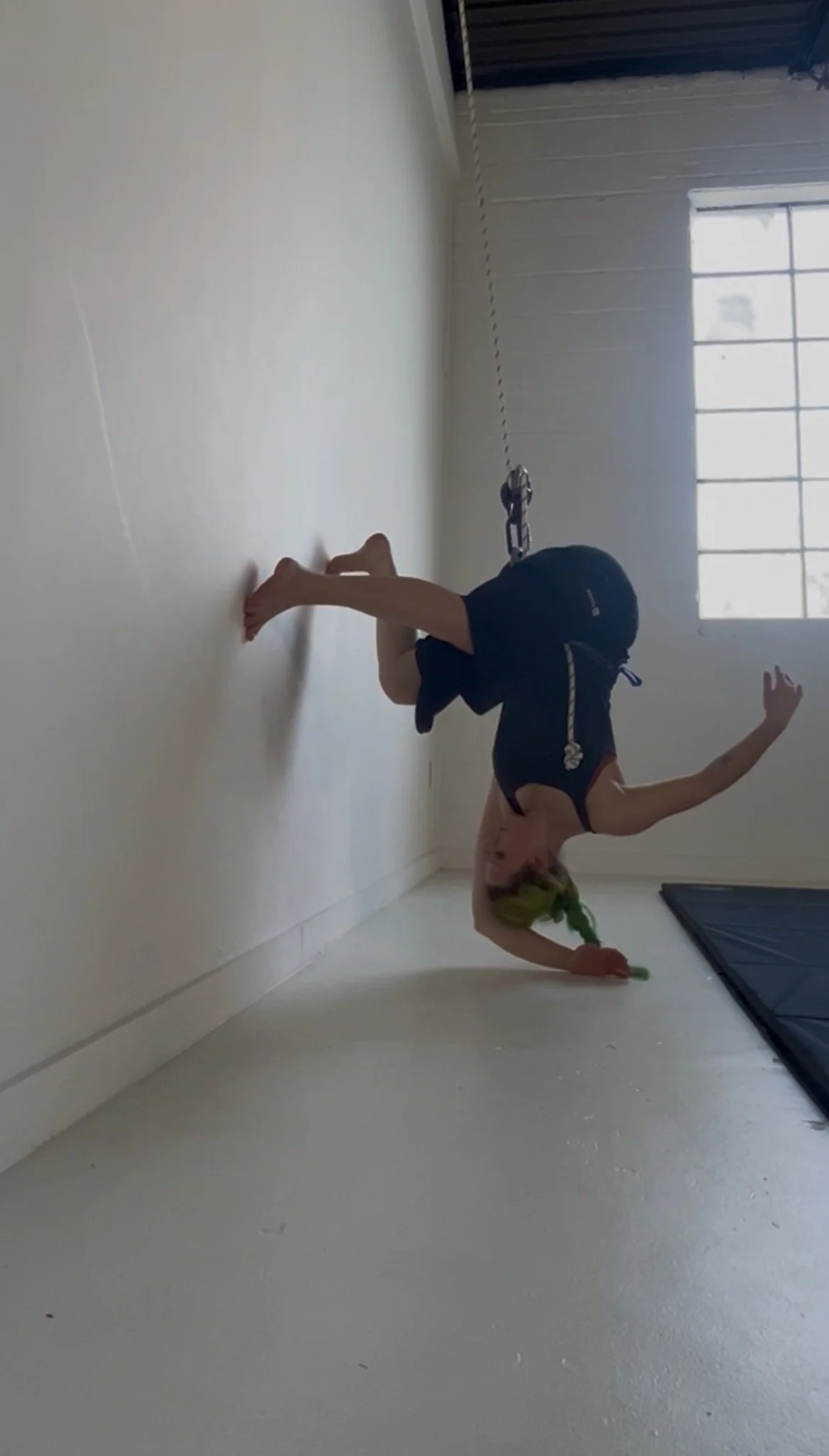woman with green hair dancing upside down with feet on a wall and one hand on the floor