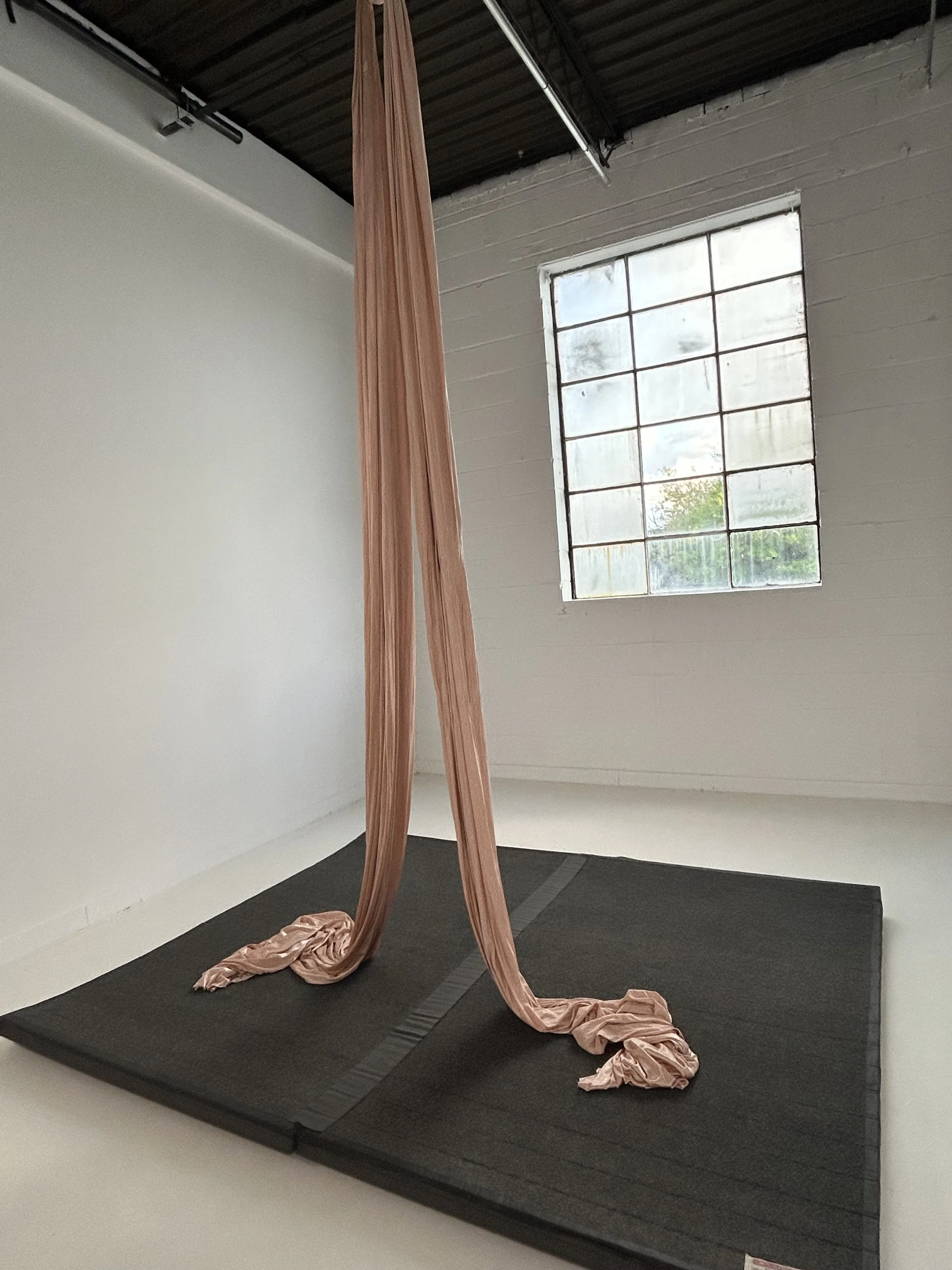 A pink silk hangs over a grey mat in a white room in front of a window