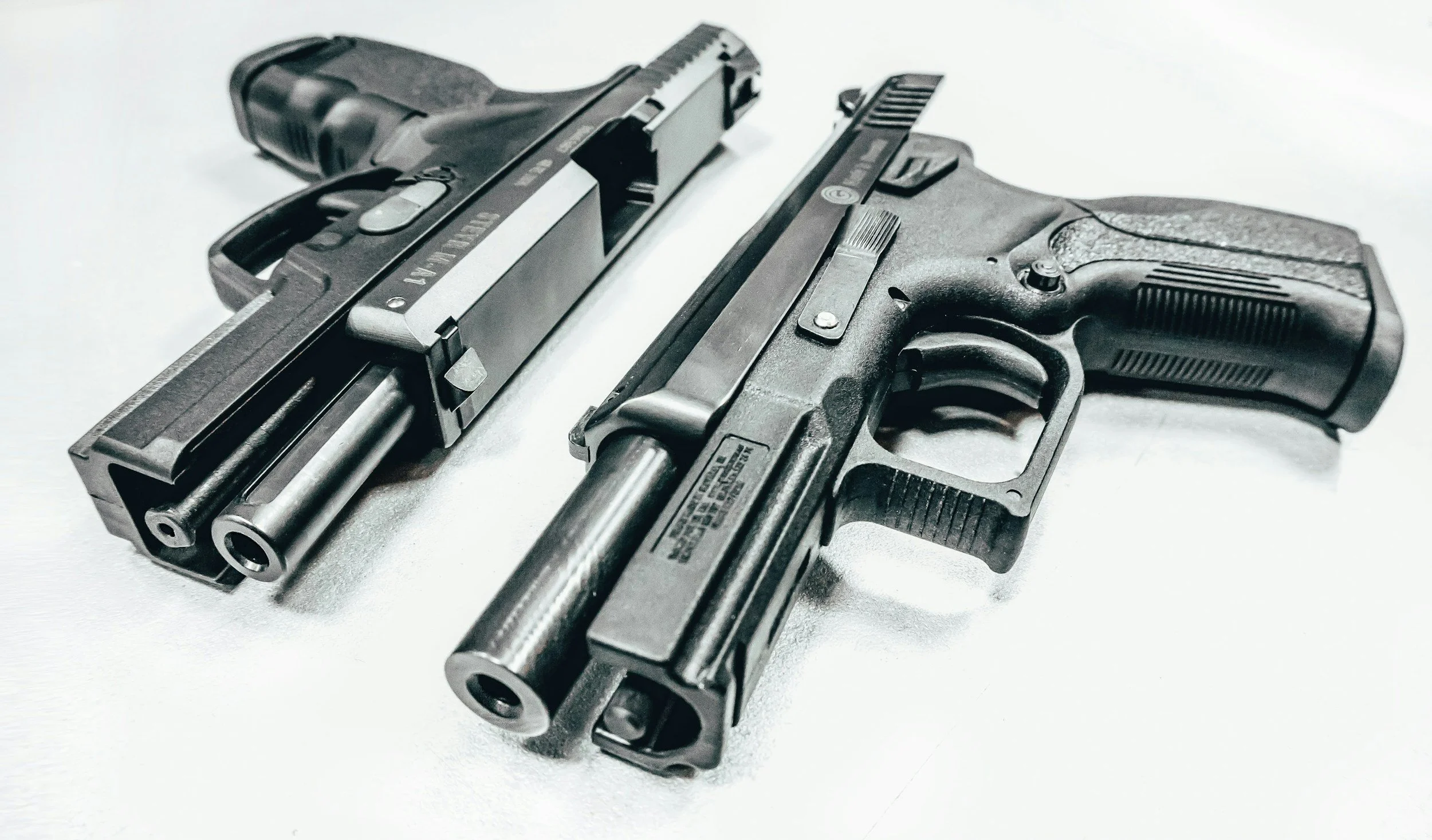 Two black semi-automatic handguns and two silver bullets on a white surface.