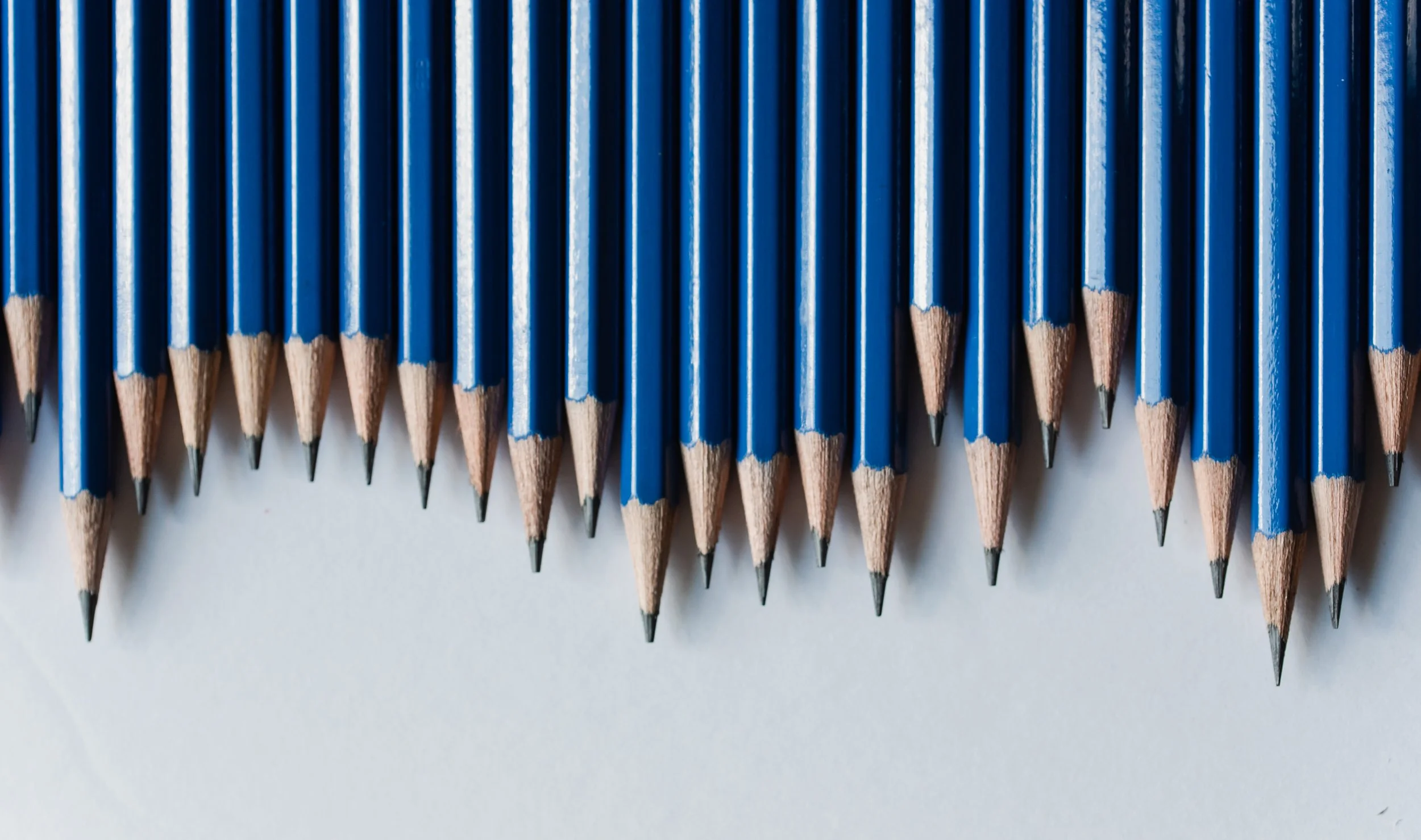 Close-up of many blue wooden pencils with sharpened tips lined up on a white surface.