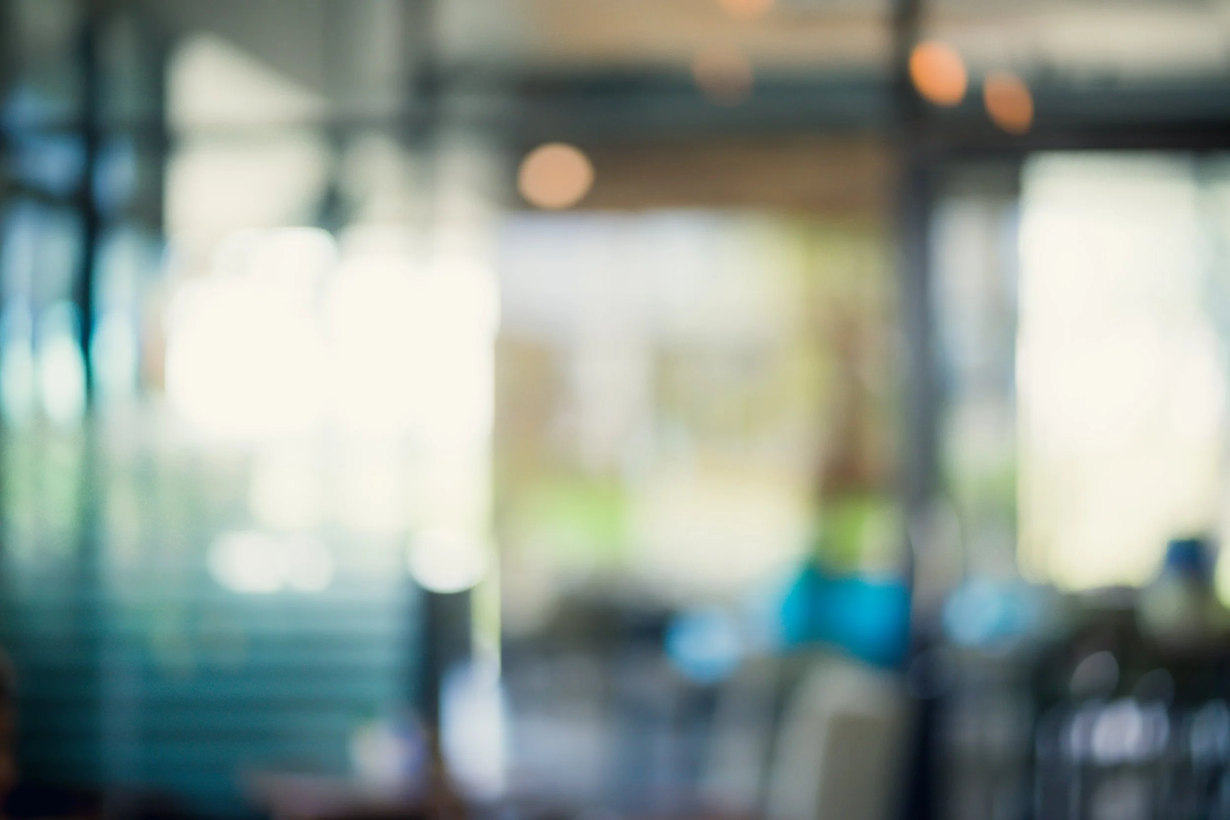 Blurred indoor scene with natural light coming through windows, showing shelves and tables.