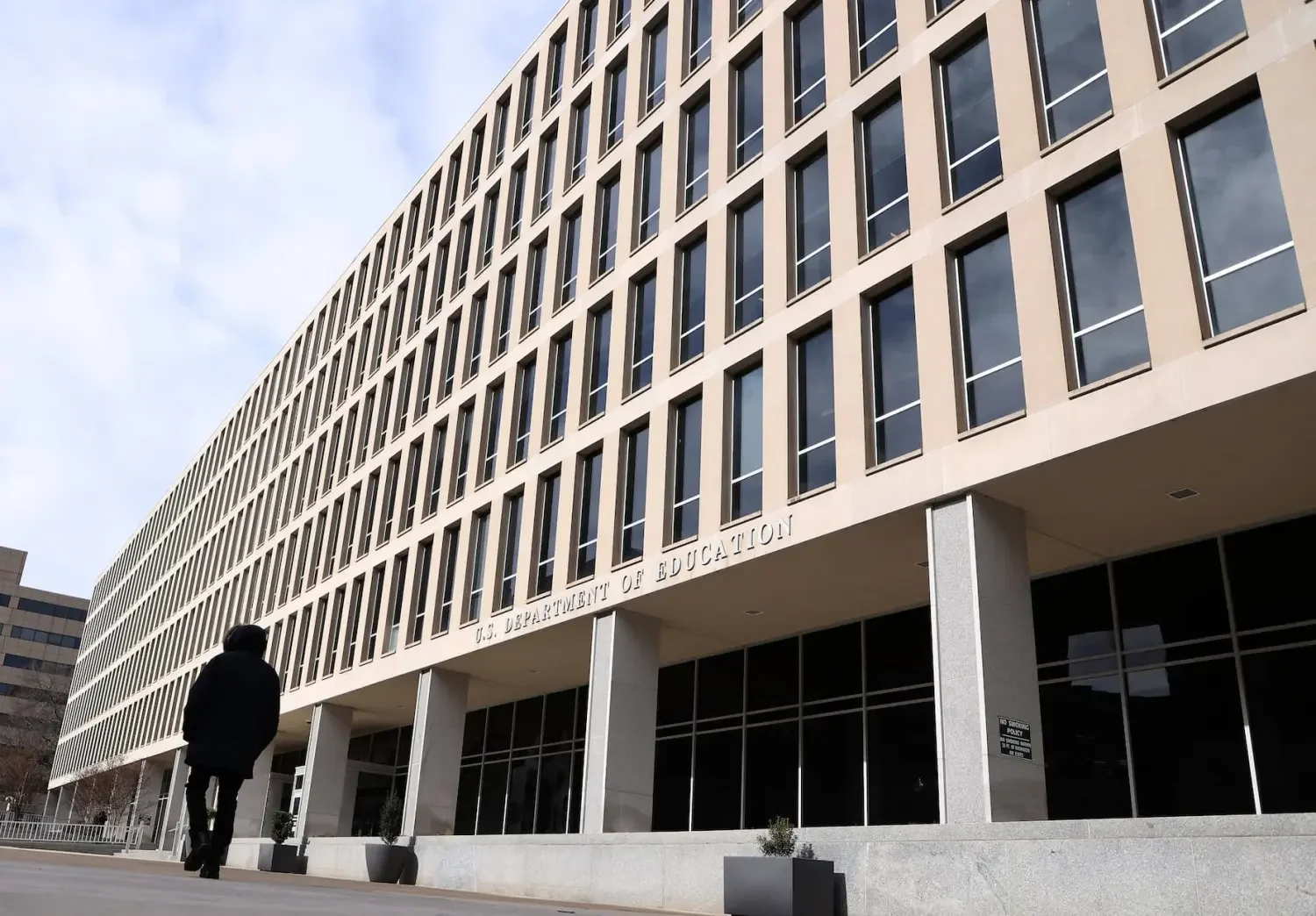 Exterior of the U.S. Department of Education building with a person walking in front.
