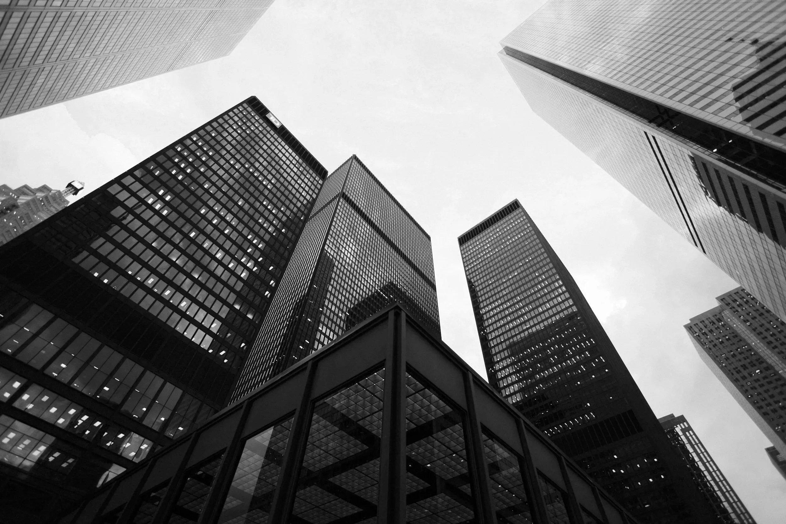 Black and white photo looking up at tall skyscrapers in a city.