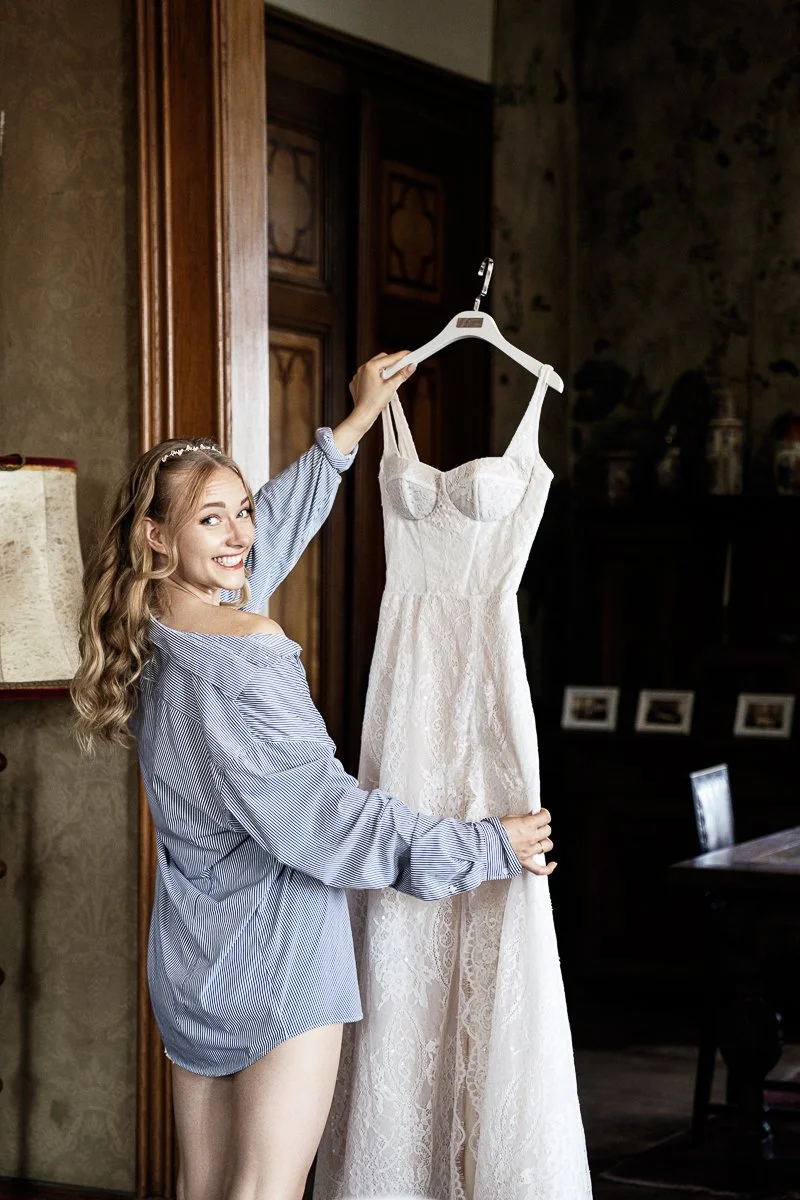 Braut hält ihr Brautkleid im Schlosszimmer von Schloss Arenfels hoch und lacht