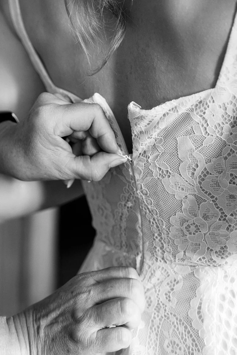 Die Knöpfe am Spitzenkleid der Braut werden geschlossen, schwarz-weiß