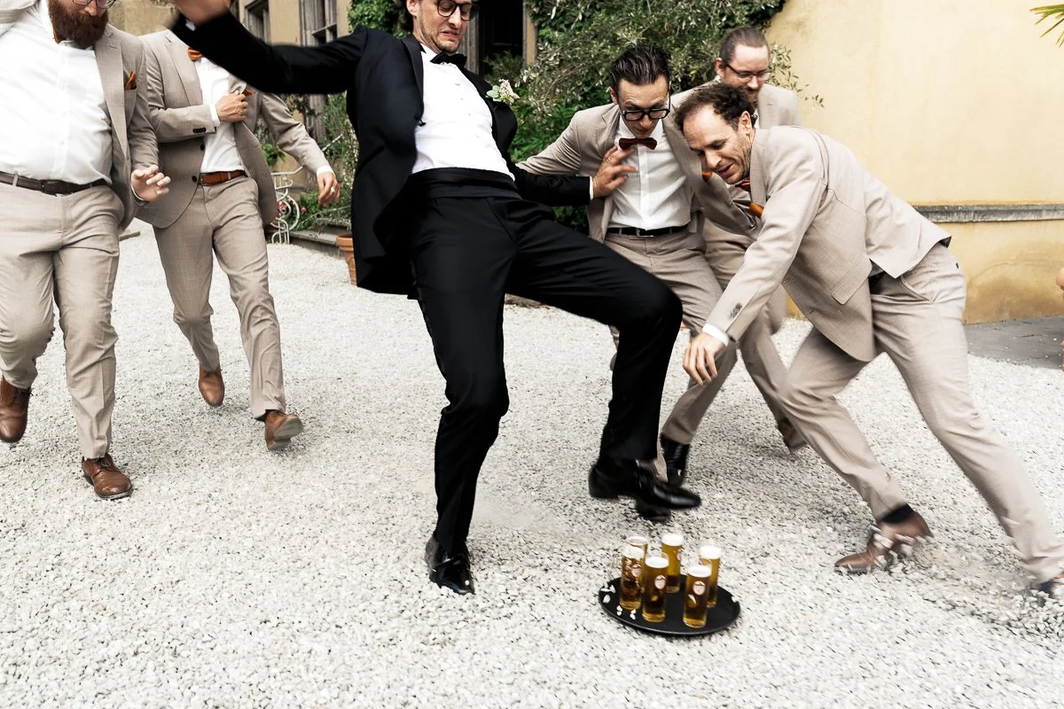 Bräutigam tanzt mit seinen Freunden um eine Flasche Champagner