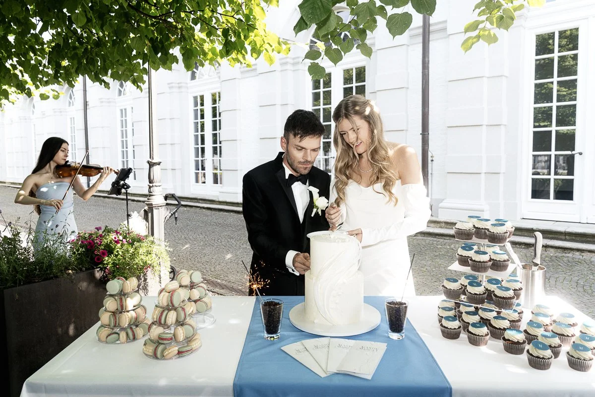 Brautpaar an der Hochzeitstorte mit Cupcakes, im Hintergrund spielt eine Geigerin