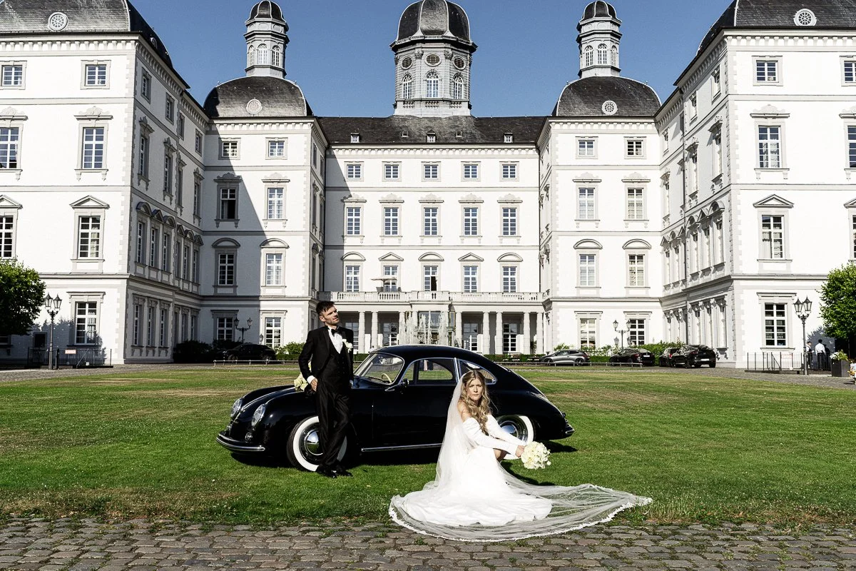 Brautpaar mit Oldtimer-Porsche auf dem Rasen vor dem Grandhotel Schloss Bensberg
