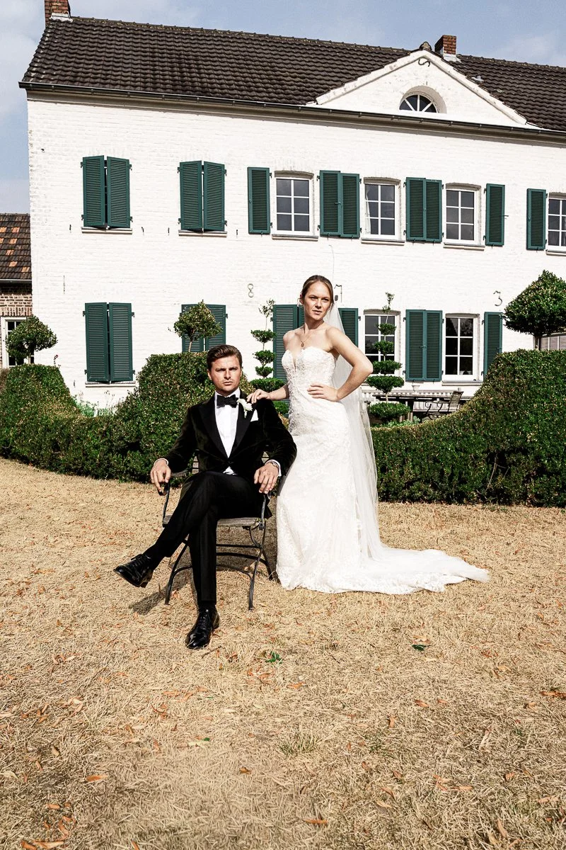 Brautpaar vor weißem Landhaus mit grünen Fensterläden bei einer Sommerhochzeit im Garten