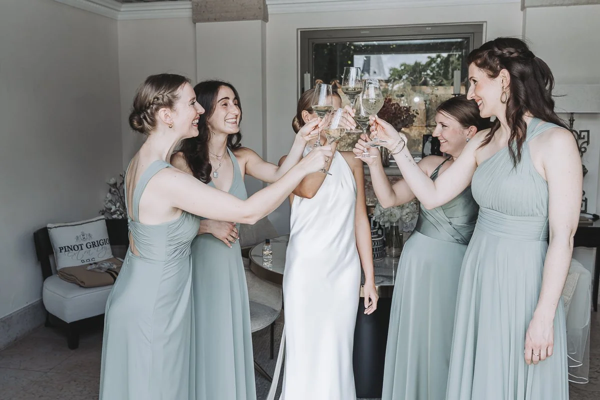 A group of women in matching light blue dresses toasting with glasses of white wine indoors.