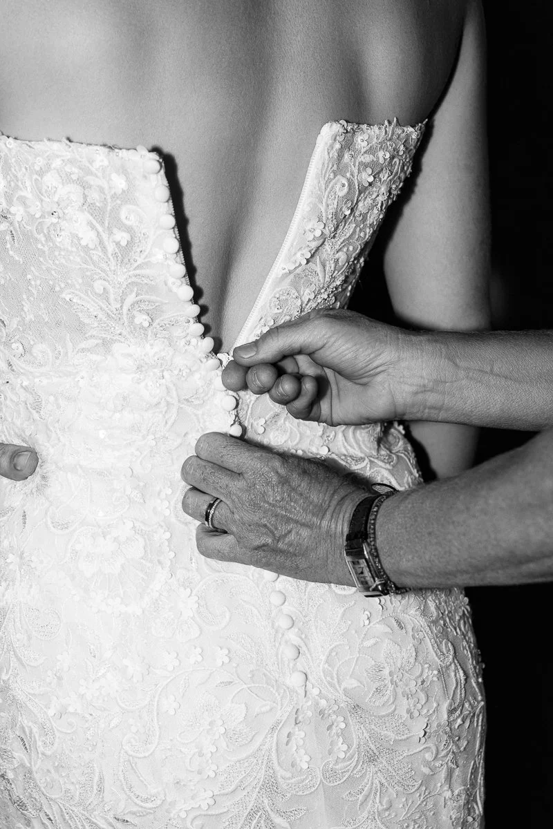 Die Knöpfe am Spitzenkleid der Braut werden geschlossen, schwarz-weiß