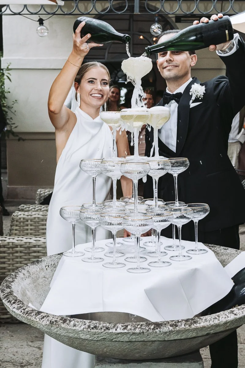 A bride and groom pouring champagne into a pyramid of glasses at their wedding reception.