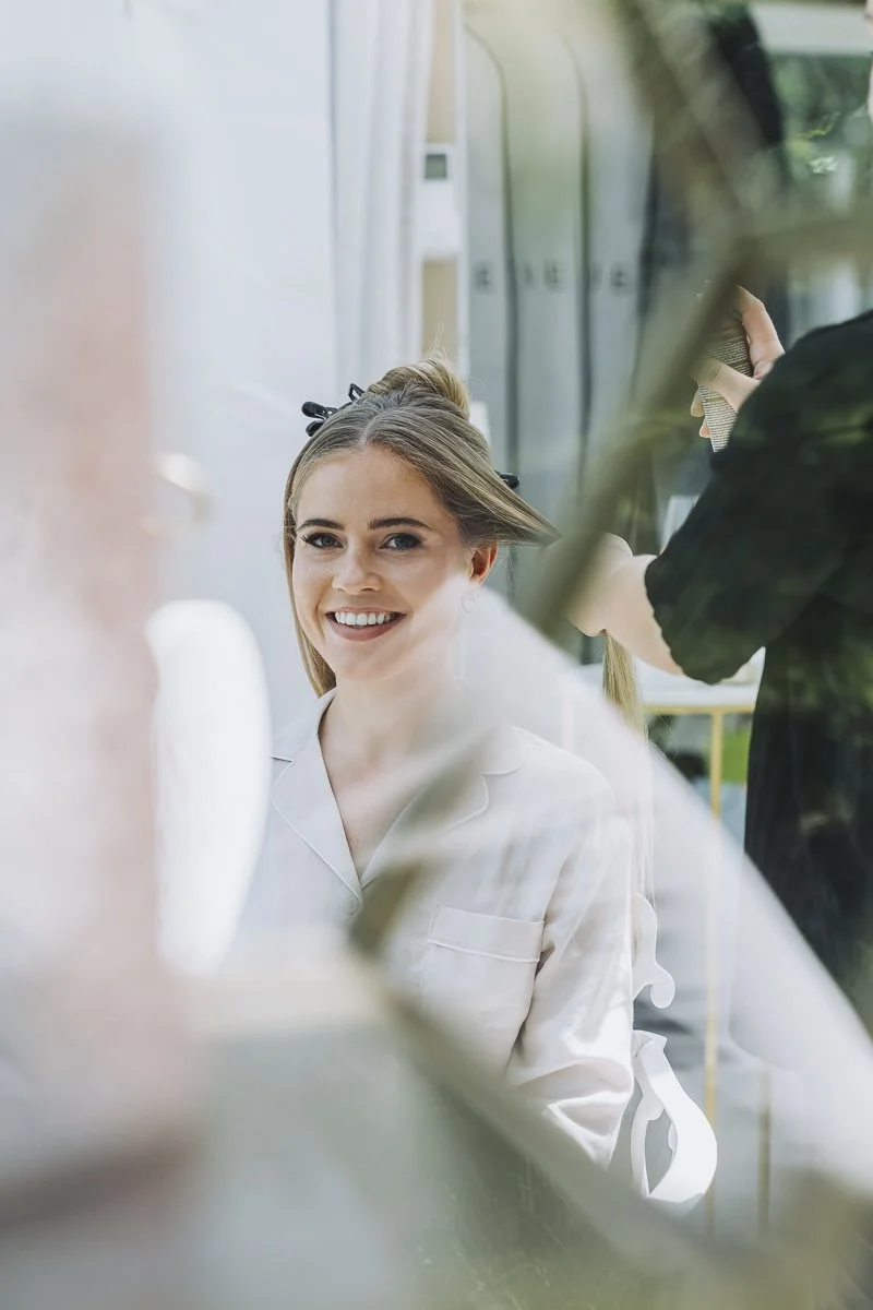 A woman smiling while getting her hair styled in a salon.