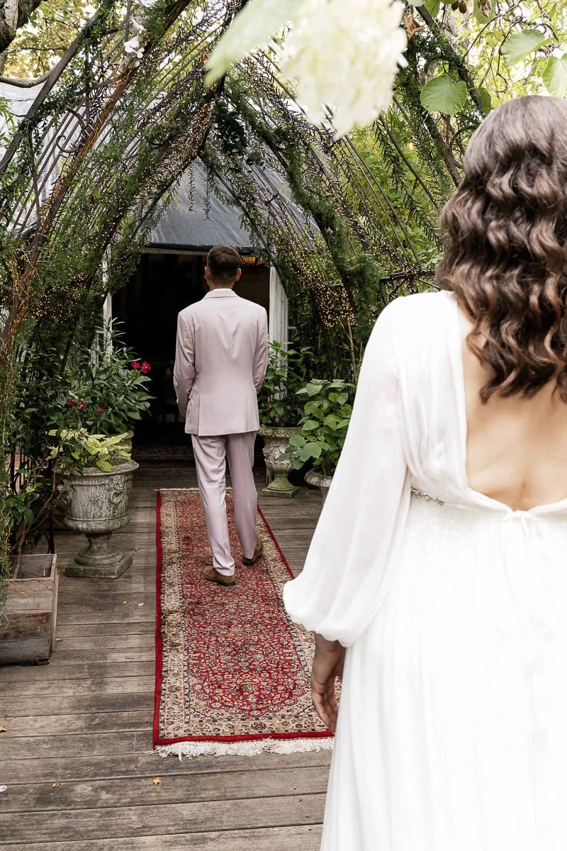 First Look: Braut geht auf den wartenden Bräutigam im grünen Wintergarten zu