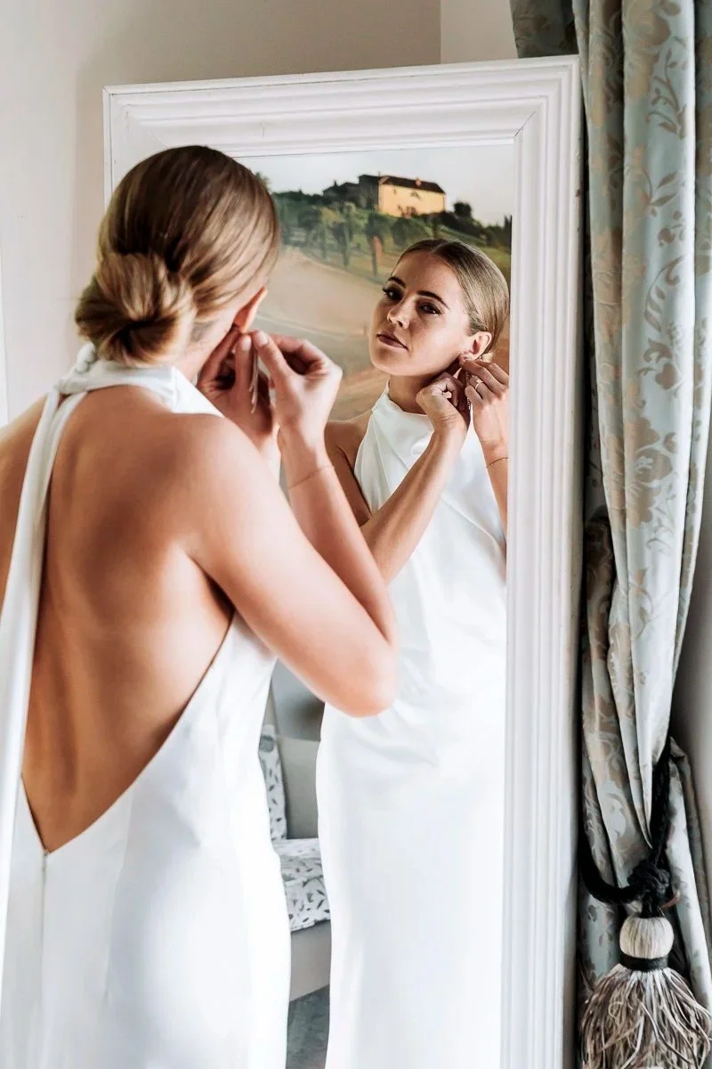 Braut richtet ihren Ohrring vor dem Spiegel beim Getting Ready am Hochzeitsmorgen
