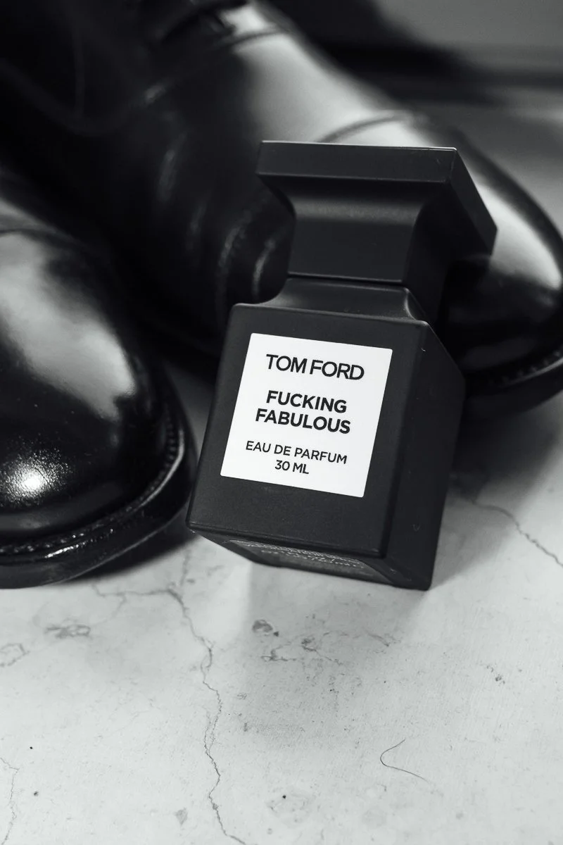 Black perfume bottle labeled 'Tom Ford Fucking Fabulous Eau De Parfum 30 ML' resting on a white cracked surface with black shoes nearby.