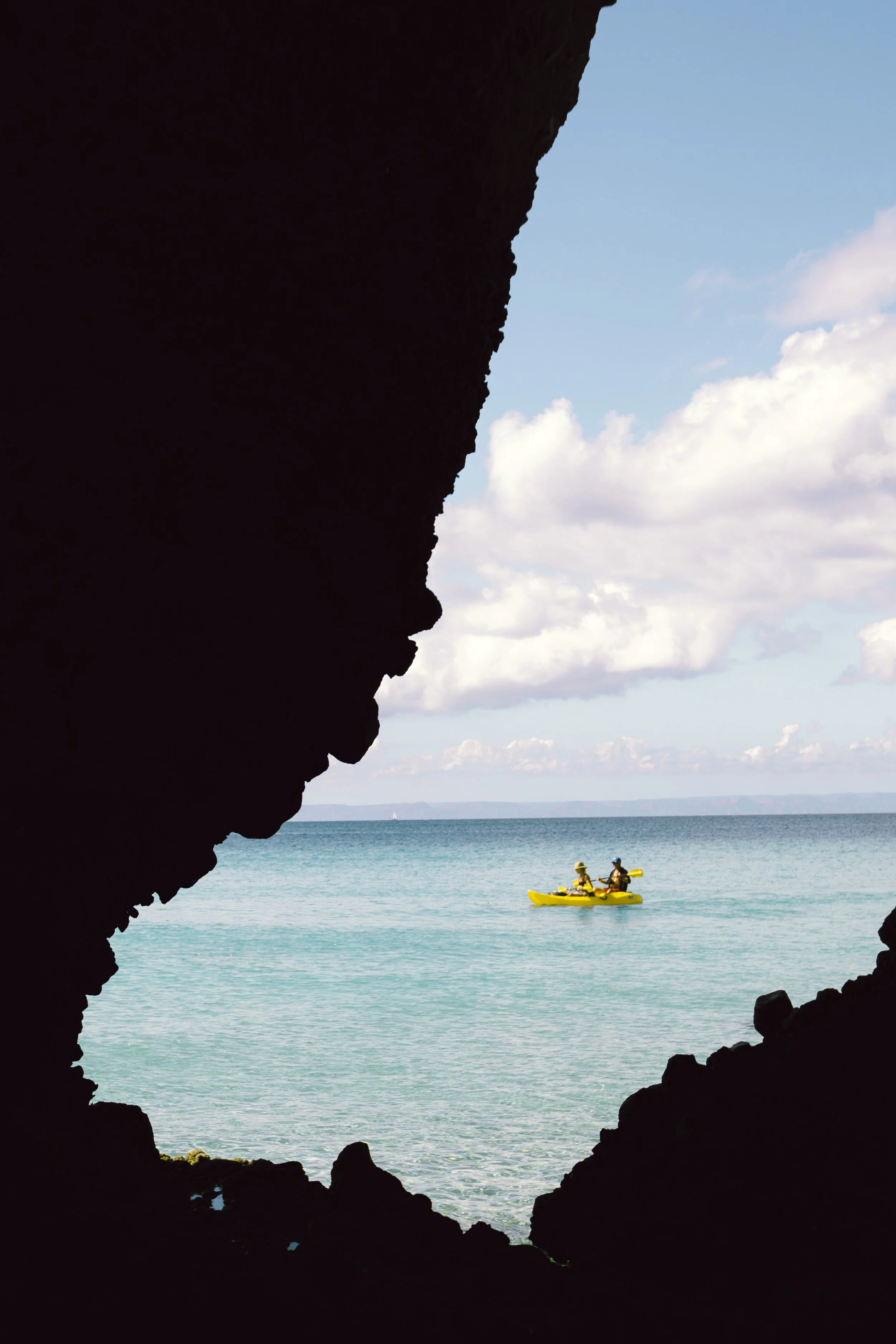 View of two people kayaking in the ocean, seen from inside a dark cave opening.