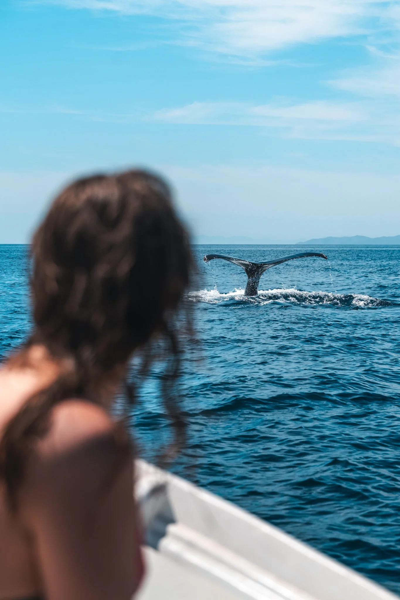 A person with wavy brown hair observing a whale's tail in the ocean