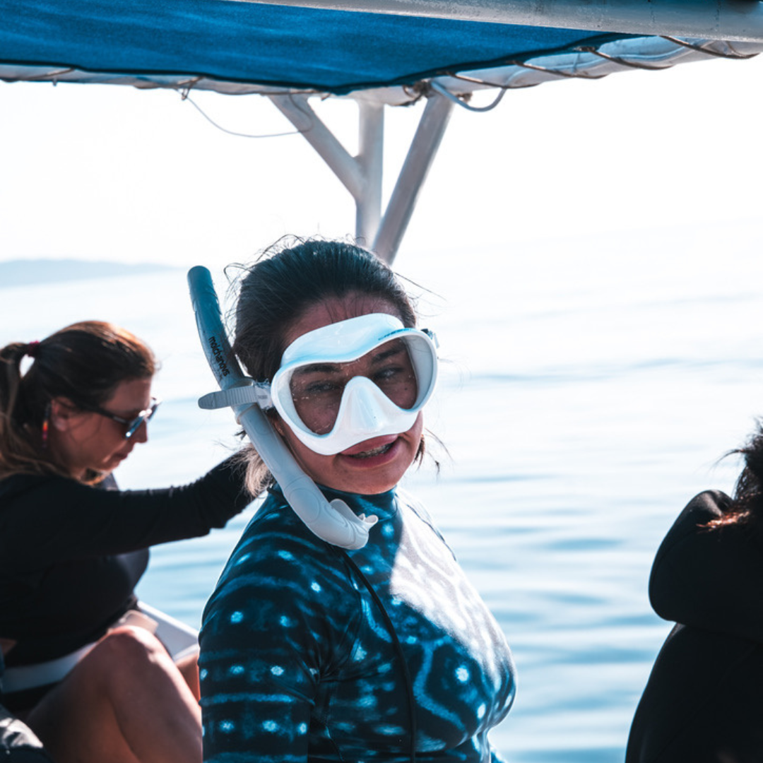 Woman in snorkeling gear on boat with other people, water in background.