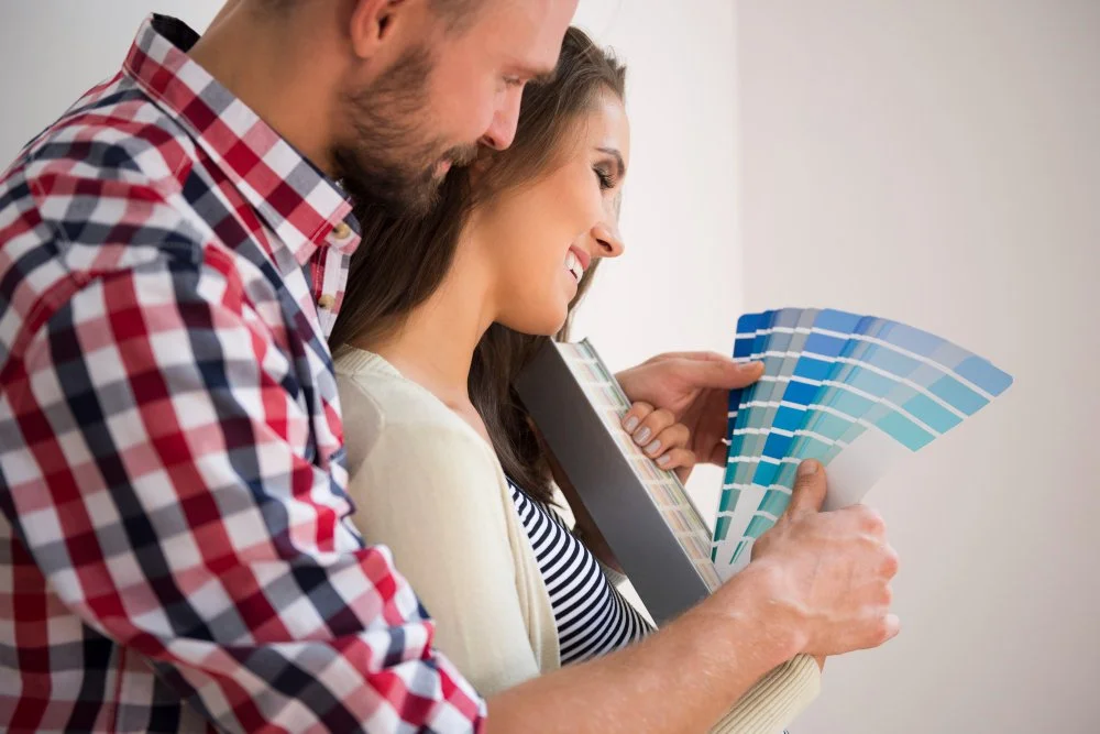 A couple in casual clothing looking at color swatches in a store or home improvement shop, smiling and examining paint options.