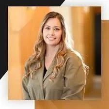 A young woman with long blonde hair smiling in an office setting.