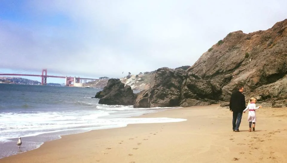 picture of father and daughter walking on the beach with the Golden Gate bridge