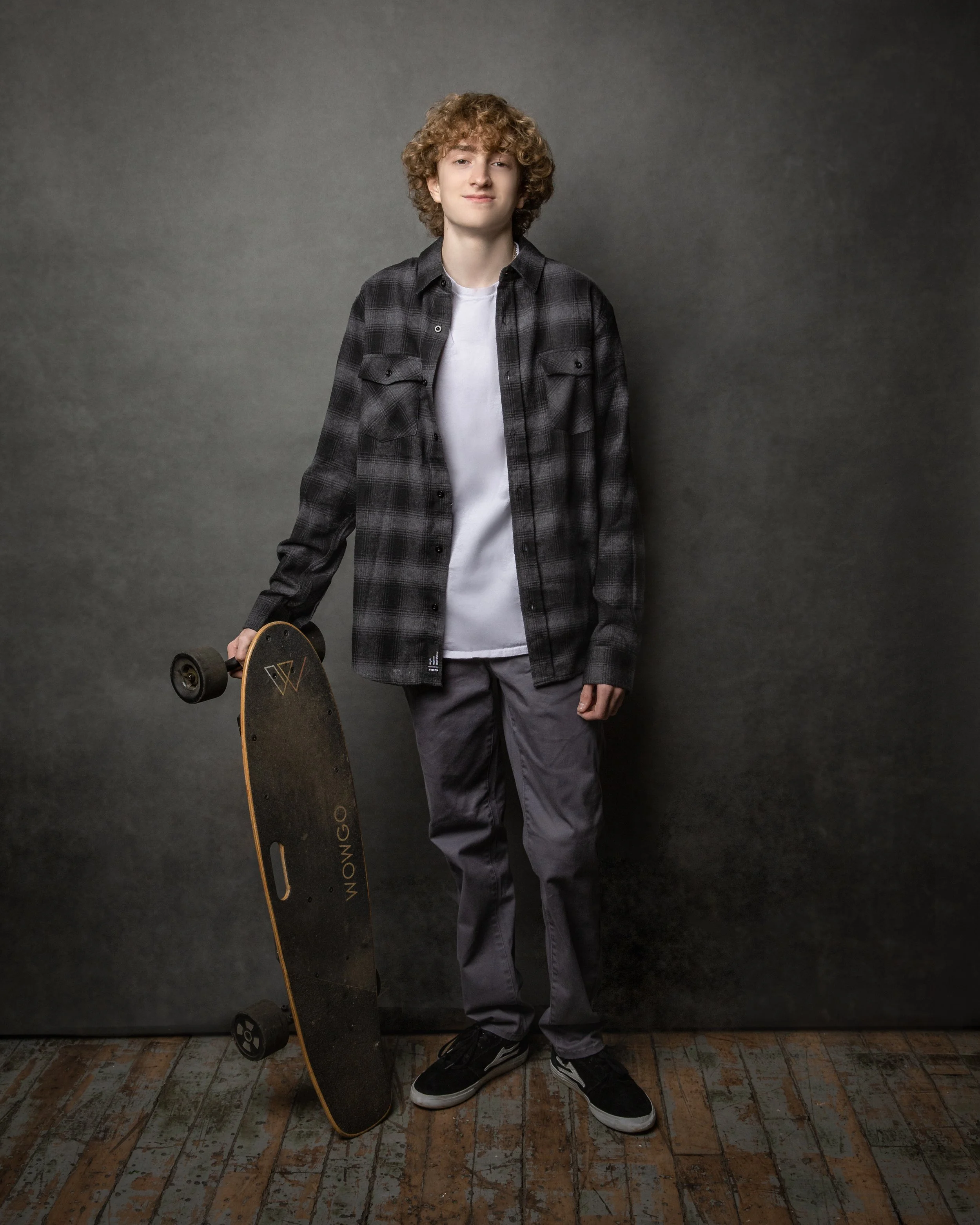 Young man holding a skateboard during a studio senior portrait session.