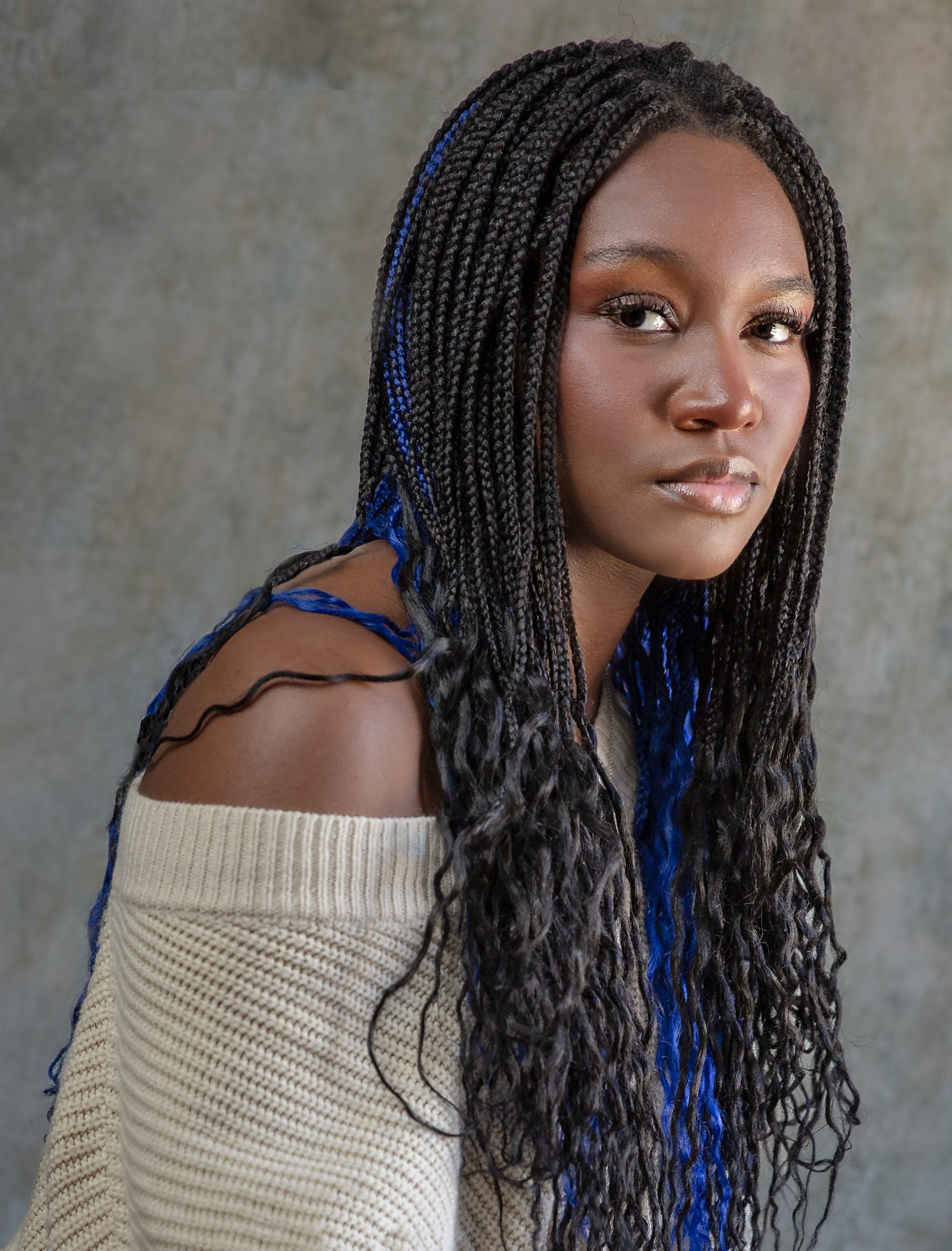 Studio senior portrait of a young woman with blue braids looking toward the camera.
