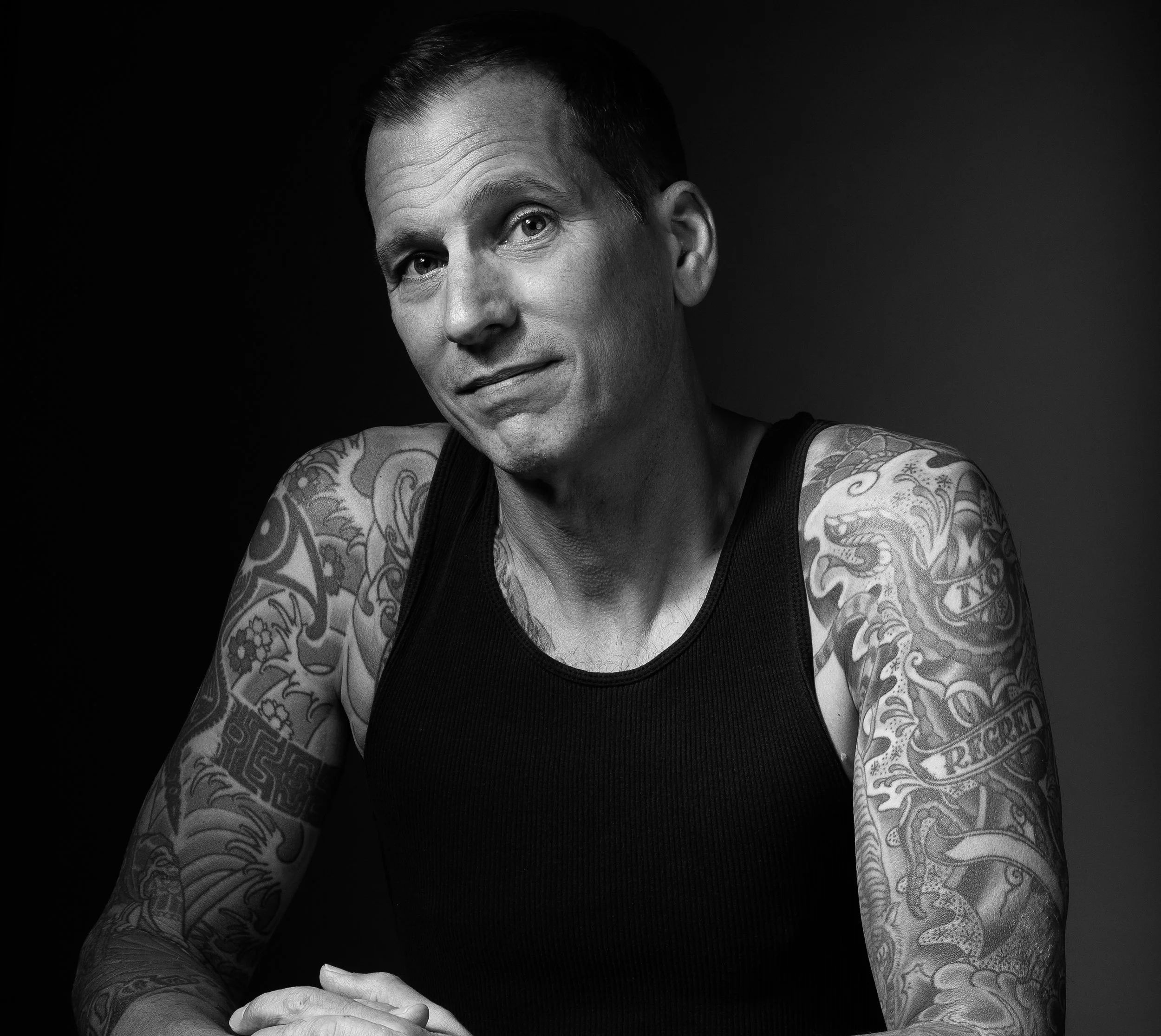 Black and white professional headshot of a tattooed man photographed in the studio with dramatic lighting.