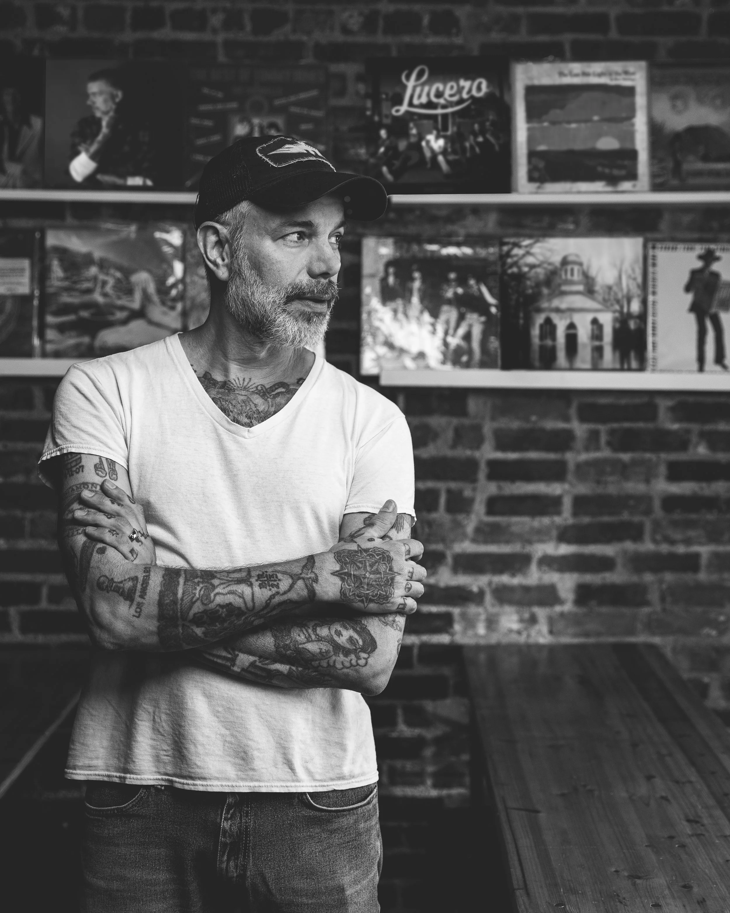 Black-and-white editorial portrait of musician Ben Nichols standing in front of a wall of Lucero records.
