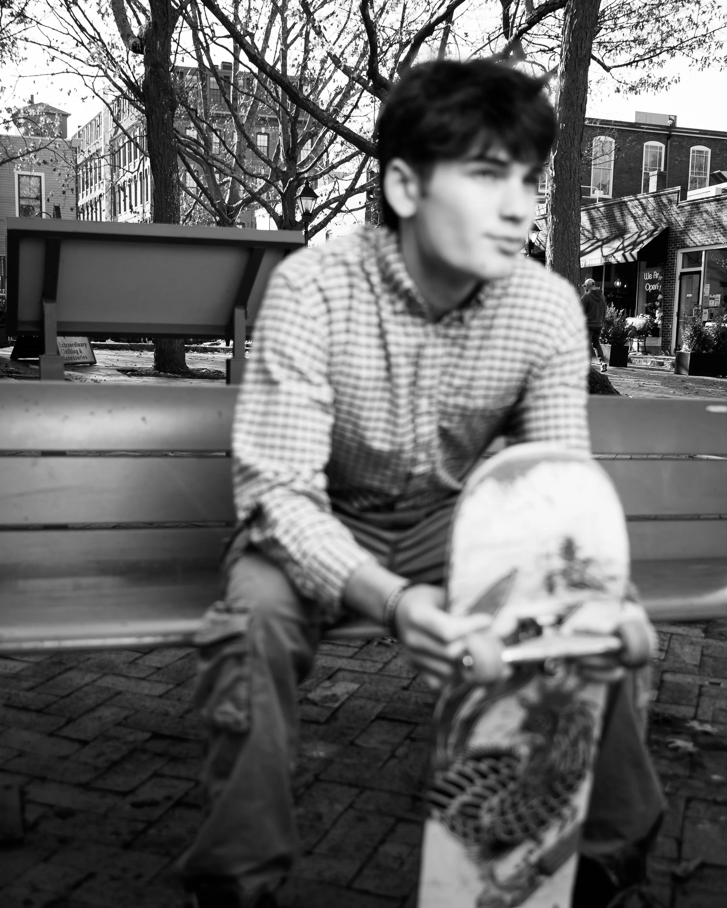 Black-and-white portrait of a young man seated on a bench with a skateboard in downtown Newburyport.