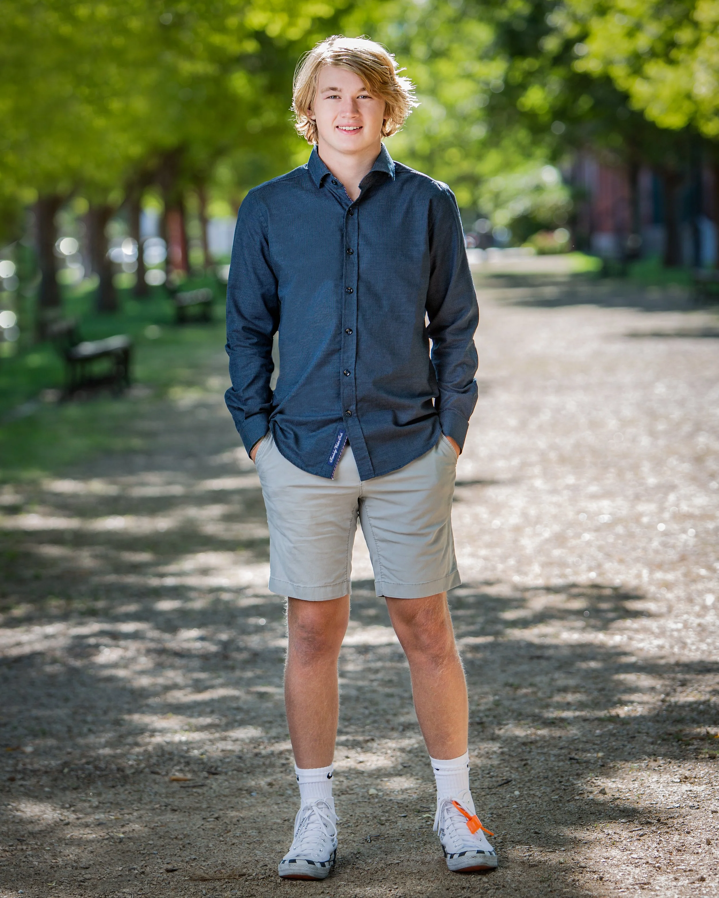 Young man standing on a tree-lined path during an outdoor senior portrait session.