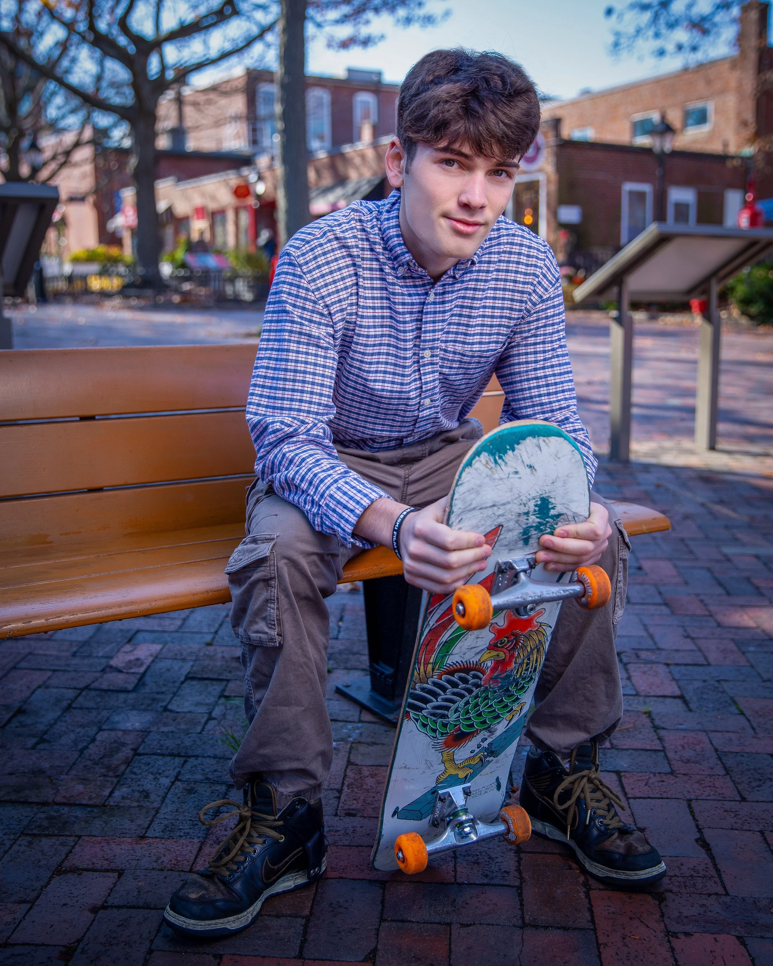 Young man sitting on a bench with a skateboard during an outdoor senior portrait session on Inn St in Newburyport, MA