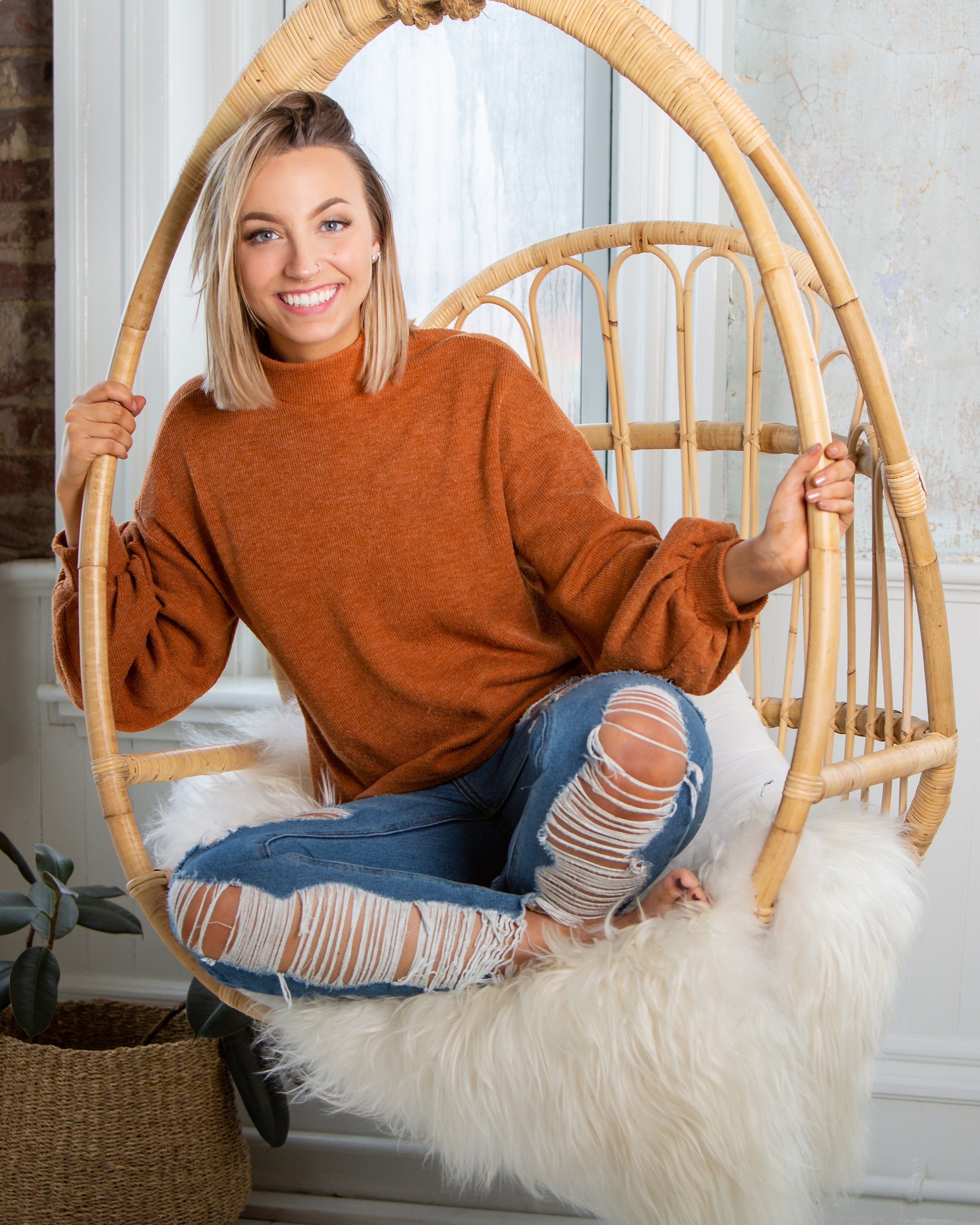 Young woman smiling in a hanging chair during an indoor senior portrait session.