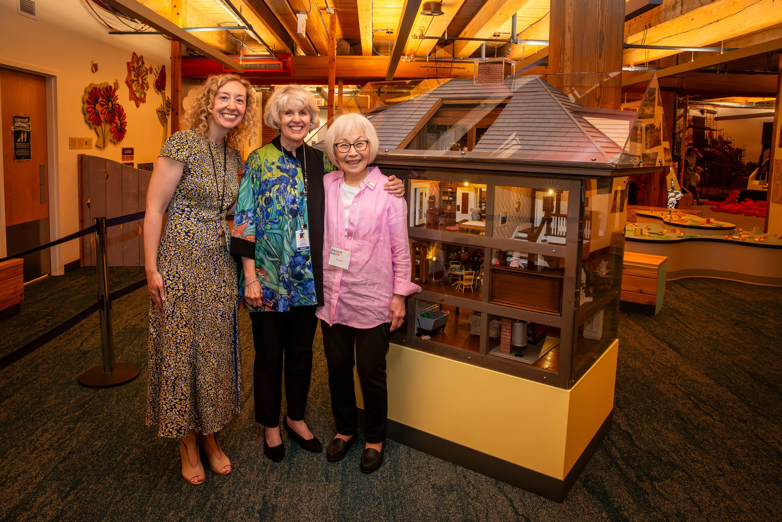 Incoming and outgoing Boston Children's Museum presidents pose with the dollhouse builder in front of her handcrafted dollhouse.