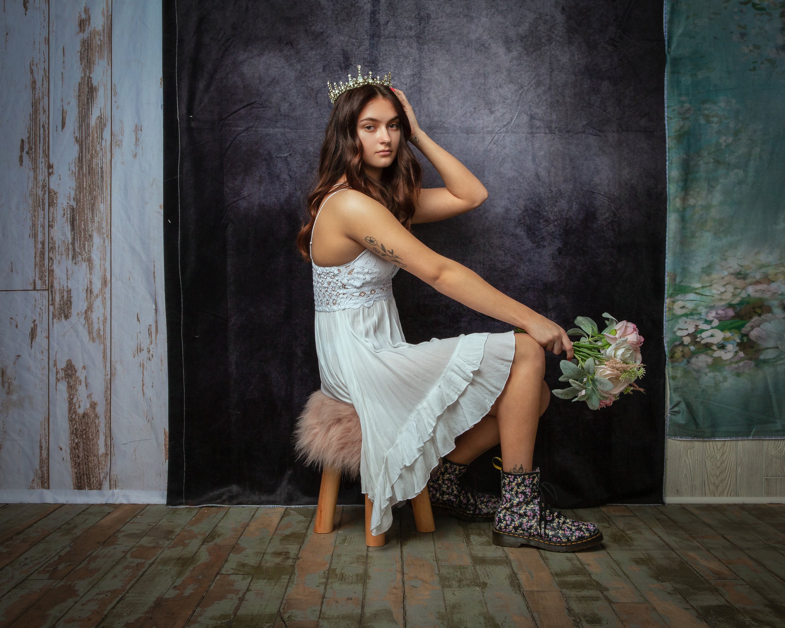 High school senior in a white dress holding a bouquet during a creative studio portrait session.