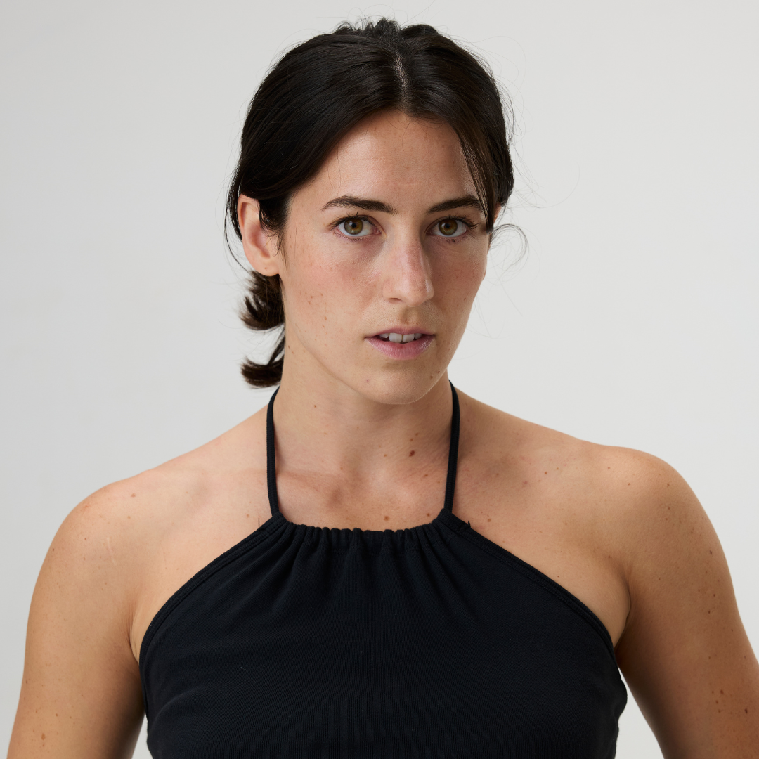A woman with dark hair and light skin wearing a black halter top, looking directly at the camera against a plain white background.