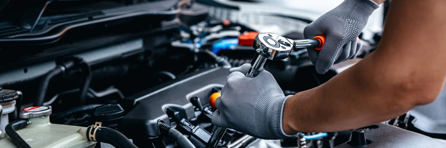 A mechanic wearing gray gloves uses a ratchet wrench to work on car engine components.