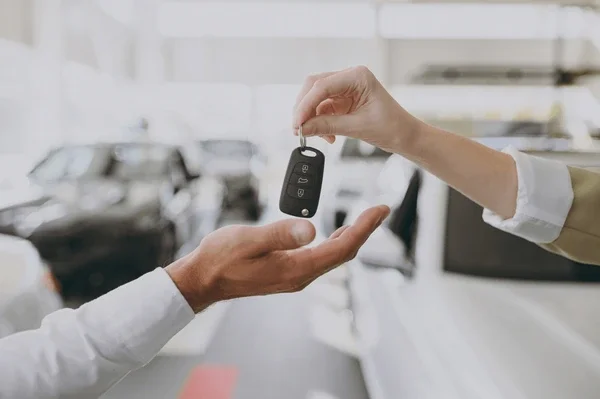 Person handing over a car key fob with buttons, in a bright indoor setting.