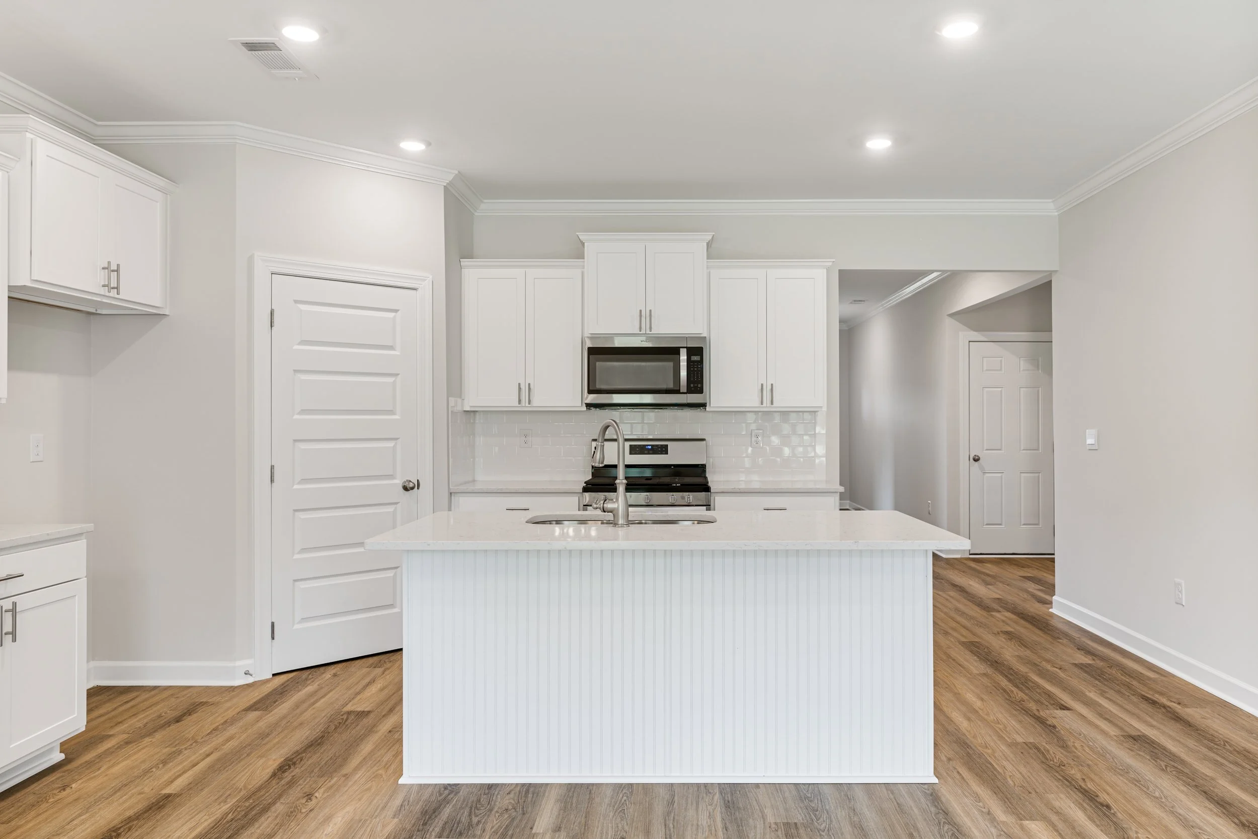 Modern white kitchen with island, stainless steel appliances, and hardwood floors.