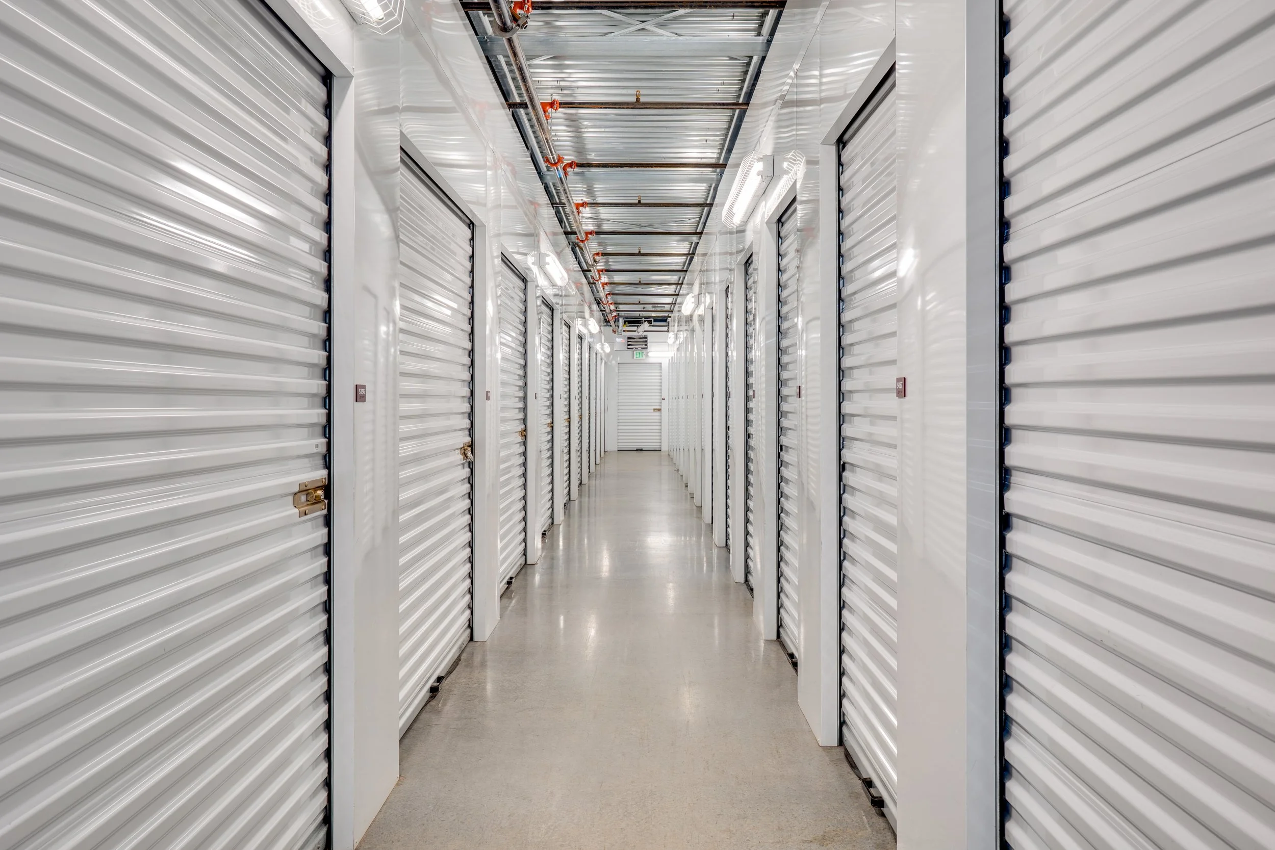 Long corridor with white storage unit doors and metal ceiling, in a self-storage facility.