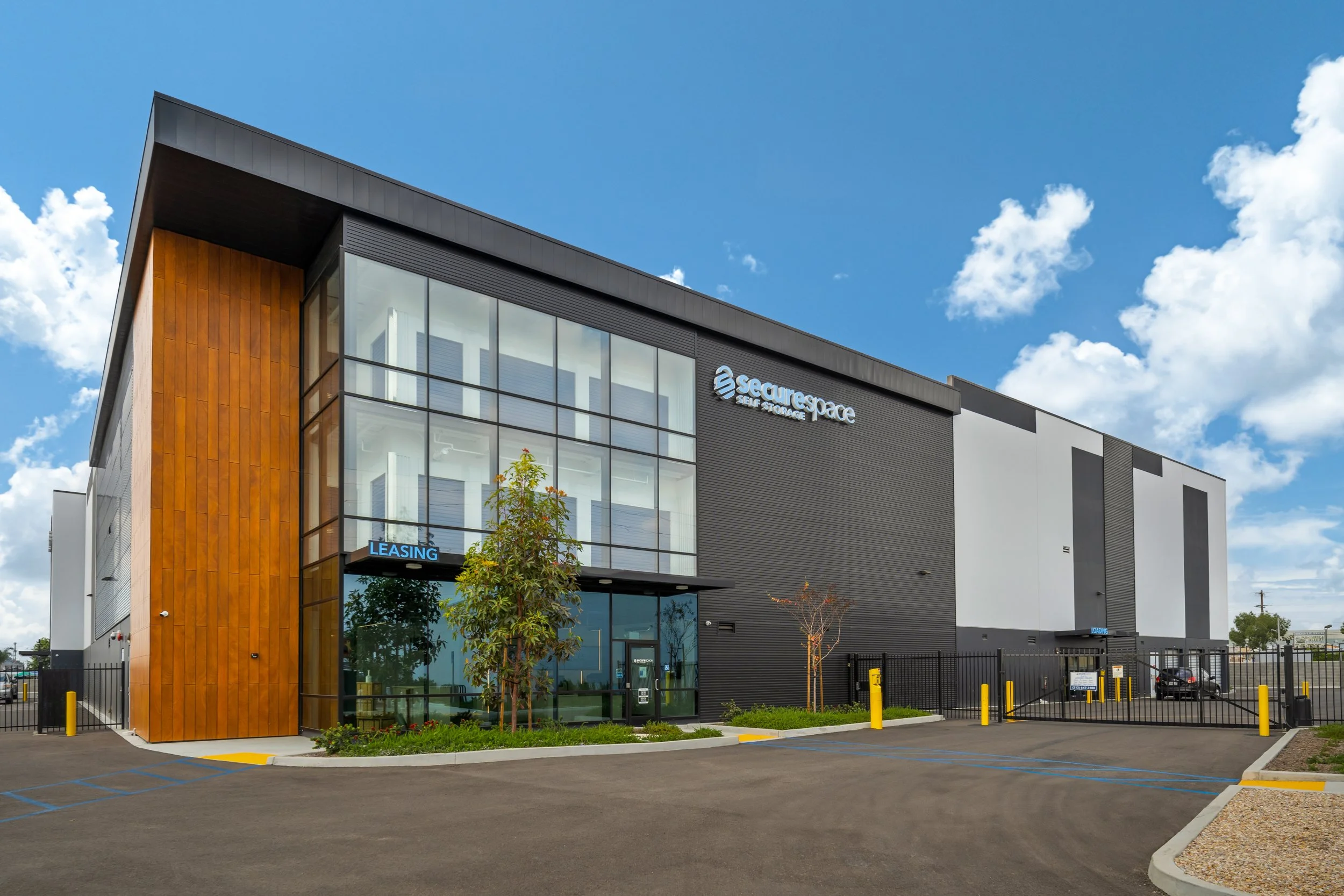 Modern commercial building with glass front and wooden accent wall, labeled 'SecureSpace' and 'Self Storage', with parking lot and security fence.