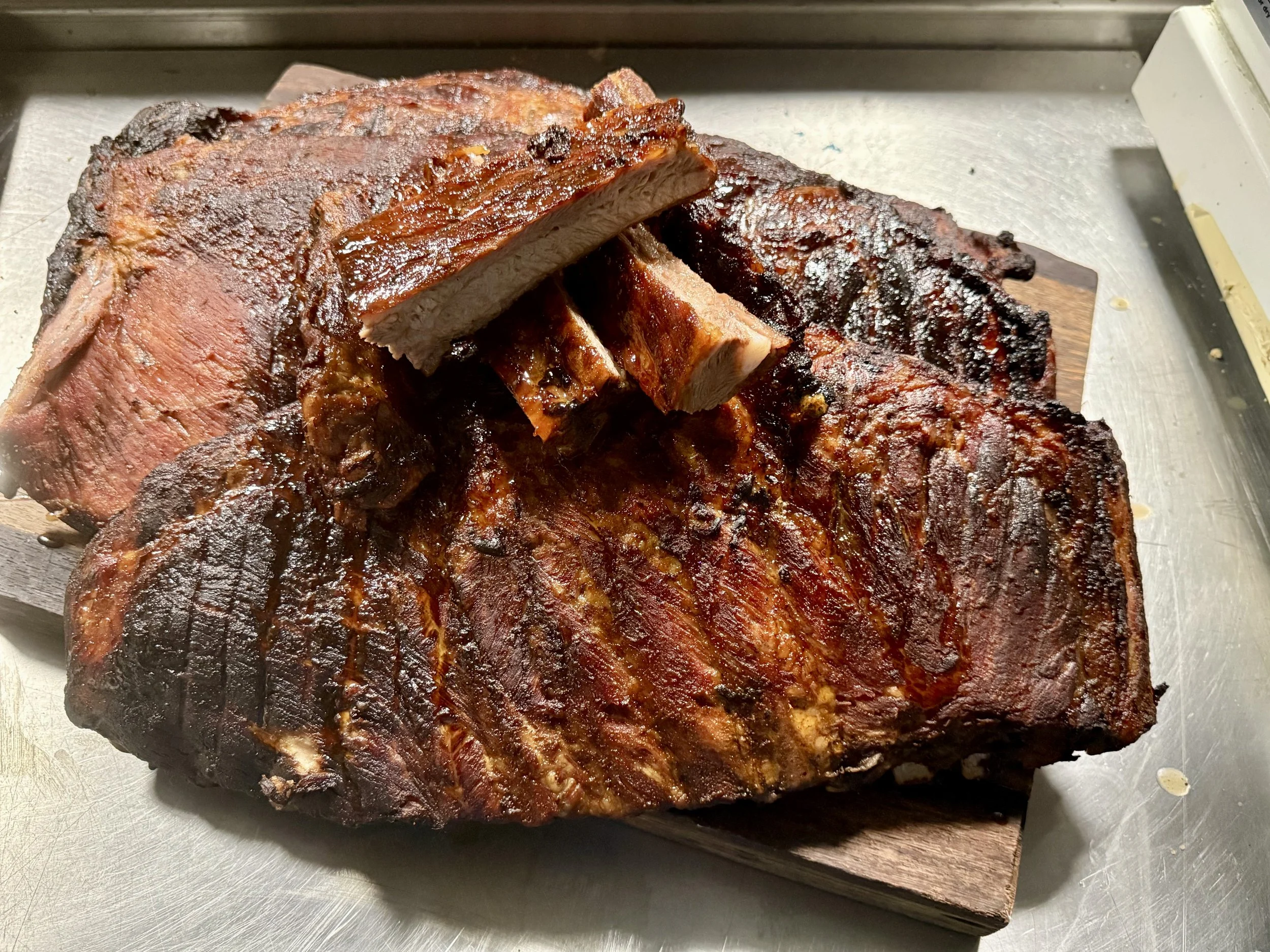 Slices of smoked barbecue ribs on a wooden cutting board, with some meat sliced and some still attached to the bone.