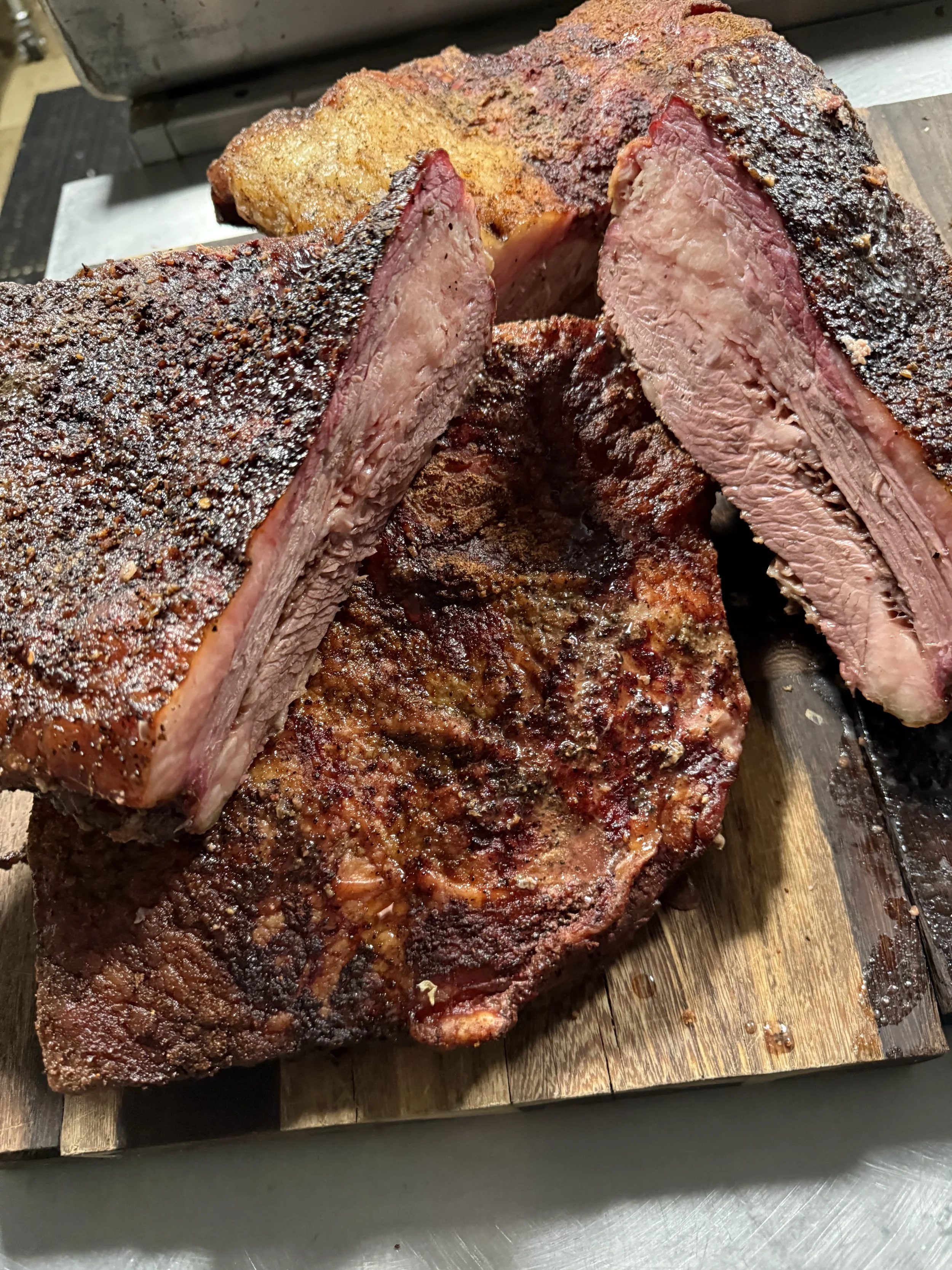 Sliced and uncut smoked beef brisket on a wooden cutting board.