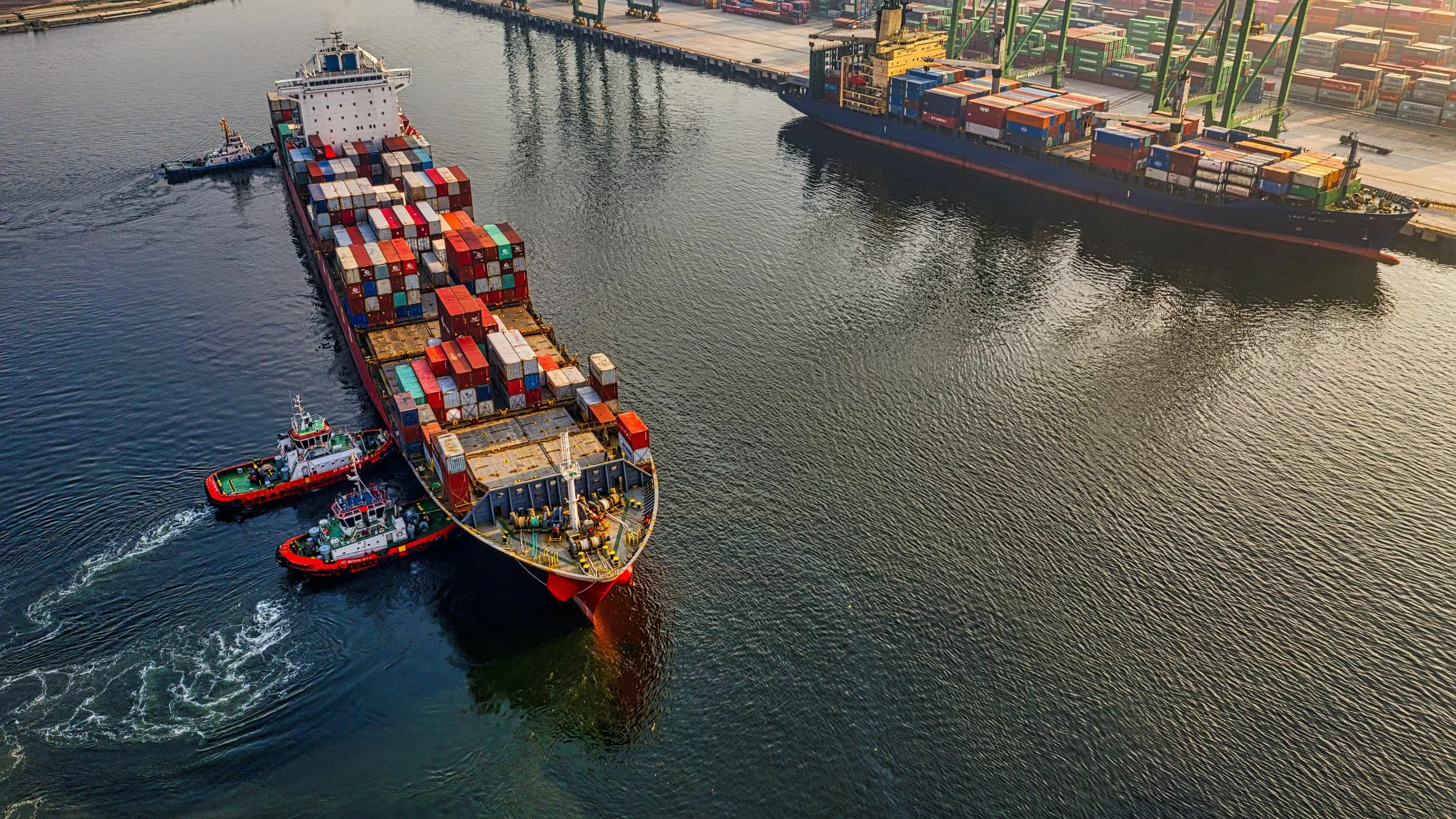 Aerial view of a container ship being guided out of port by tugboats, representing the deliberate leadership decision required to ship a product with intention and accountability.