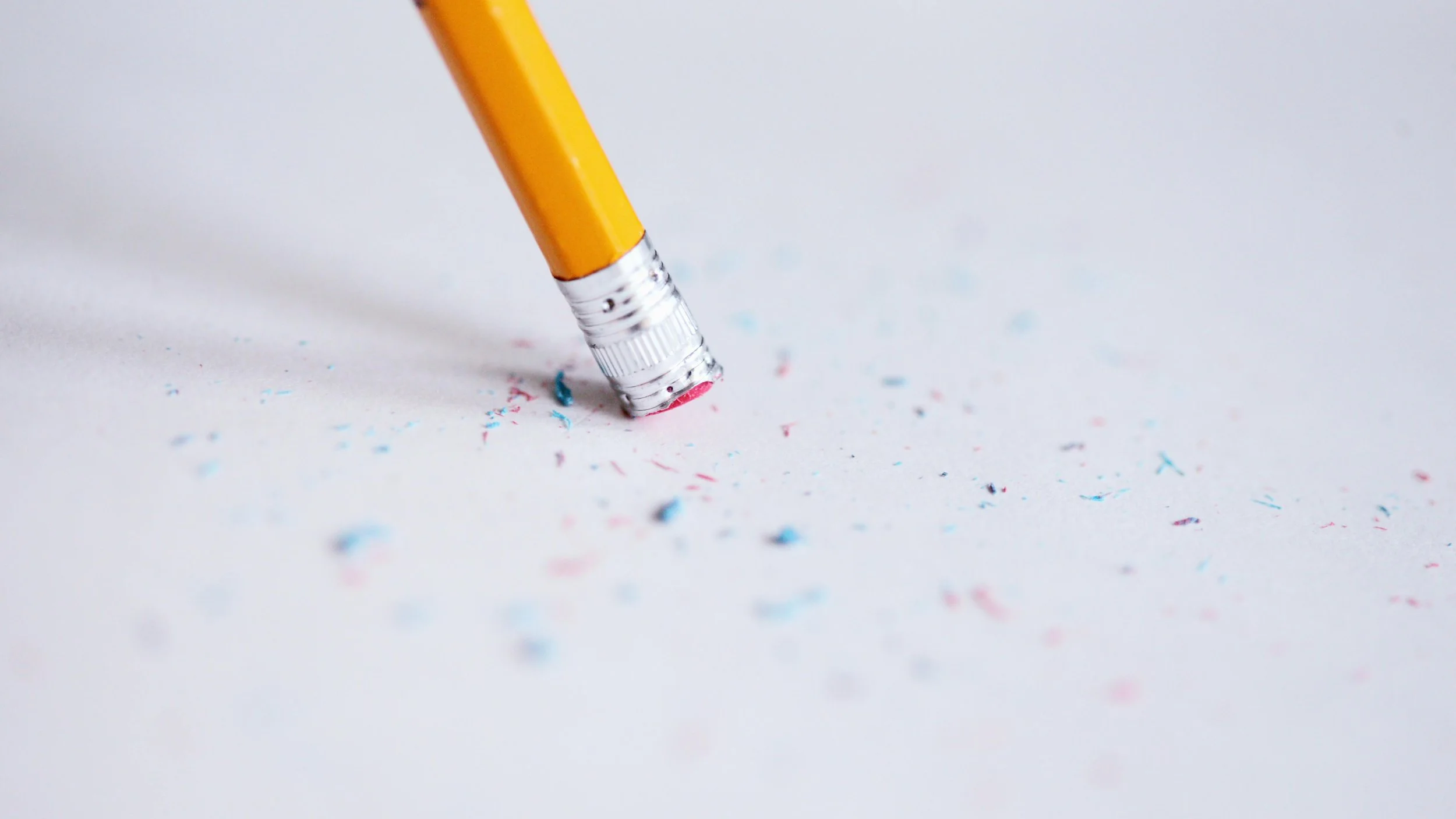 A pencil eraser actively erasing on a white surface surrounded by eraser shavings, representing how constant reprioritization quietly wears down a team's trust in the plan over time.